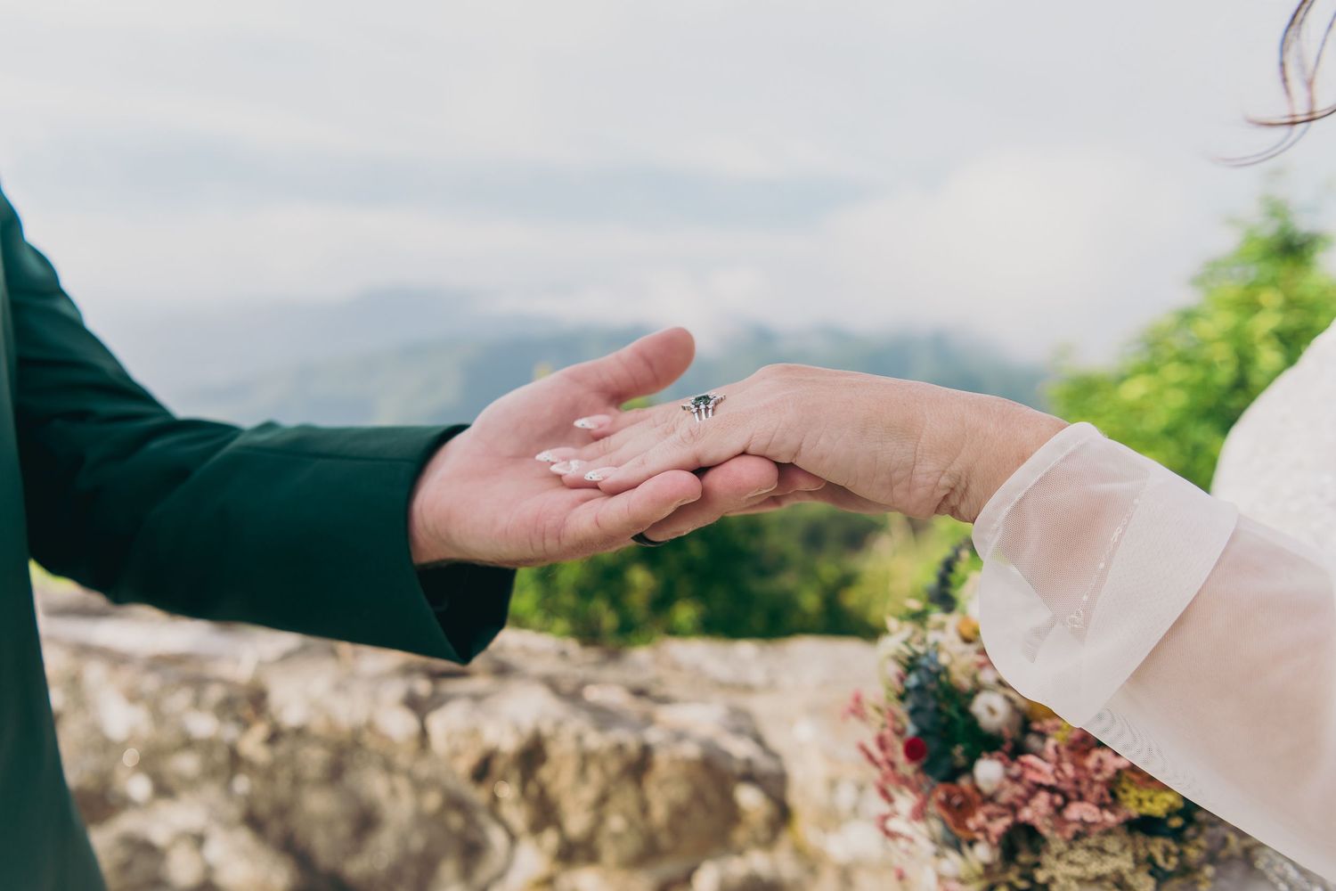 Couple exchanging wedding rings outdoors with scenic mountain views during a romantic ceremony.