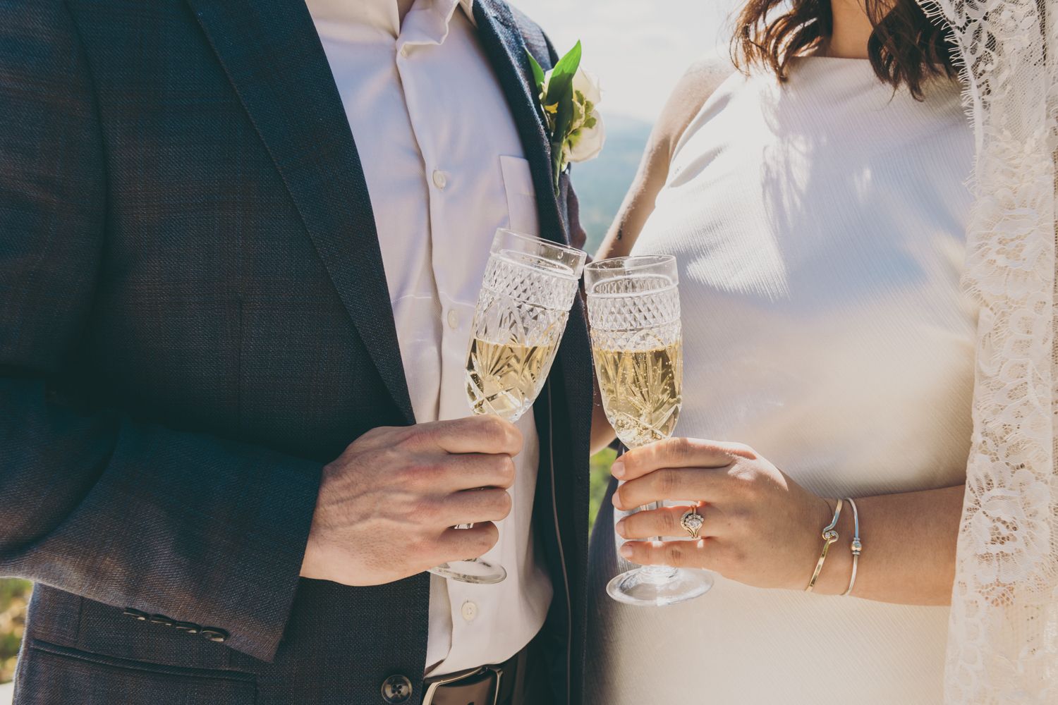 Bride and groom clinking elegant champagne glasses during wedding celebration outdoors.