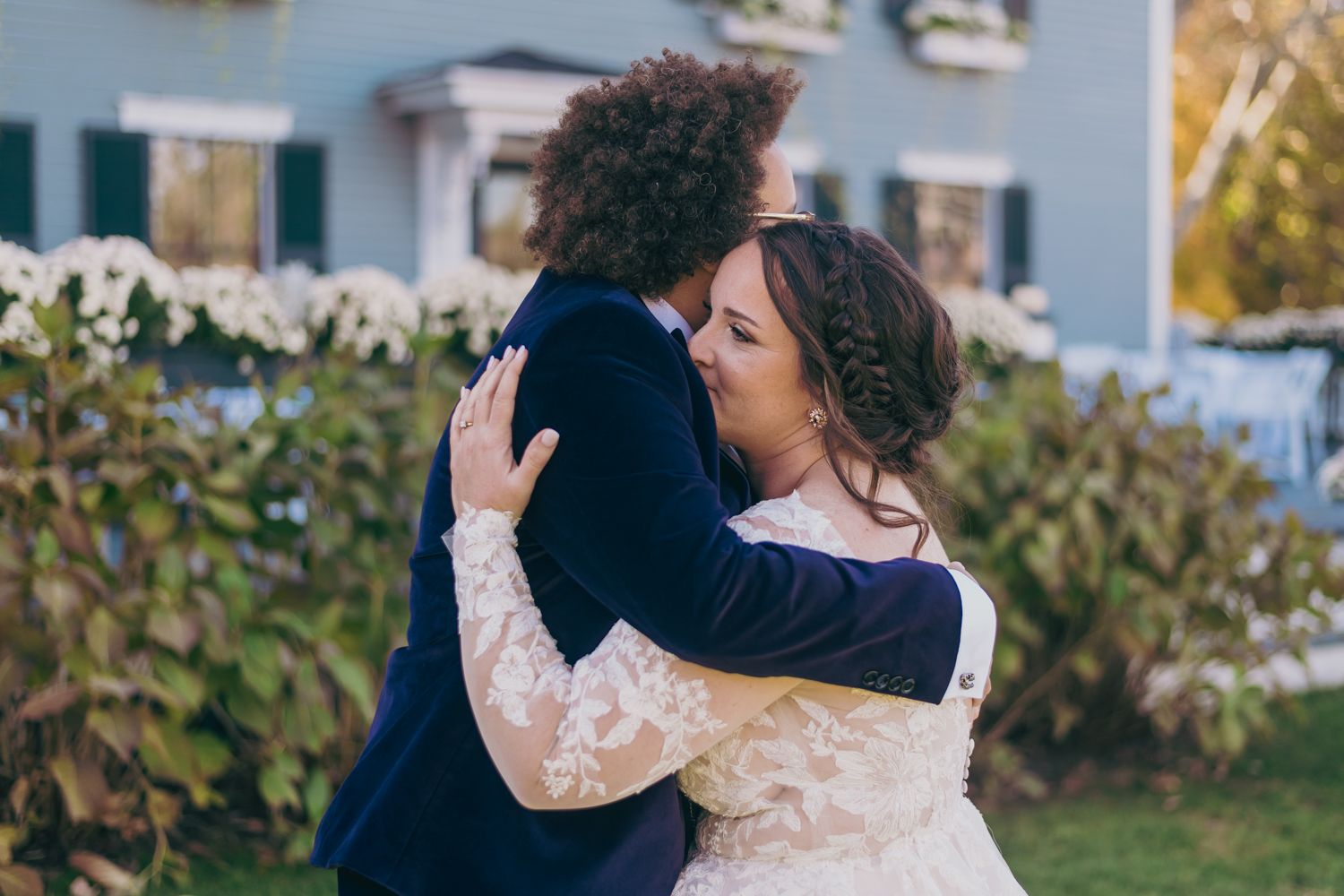 Emotional first look embrace between bride in lace gown and groom in navy suit at garden wedding.