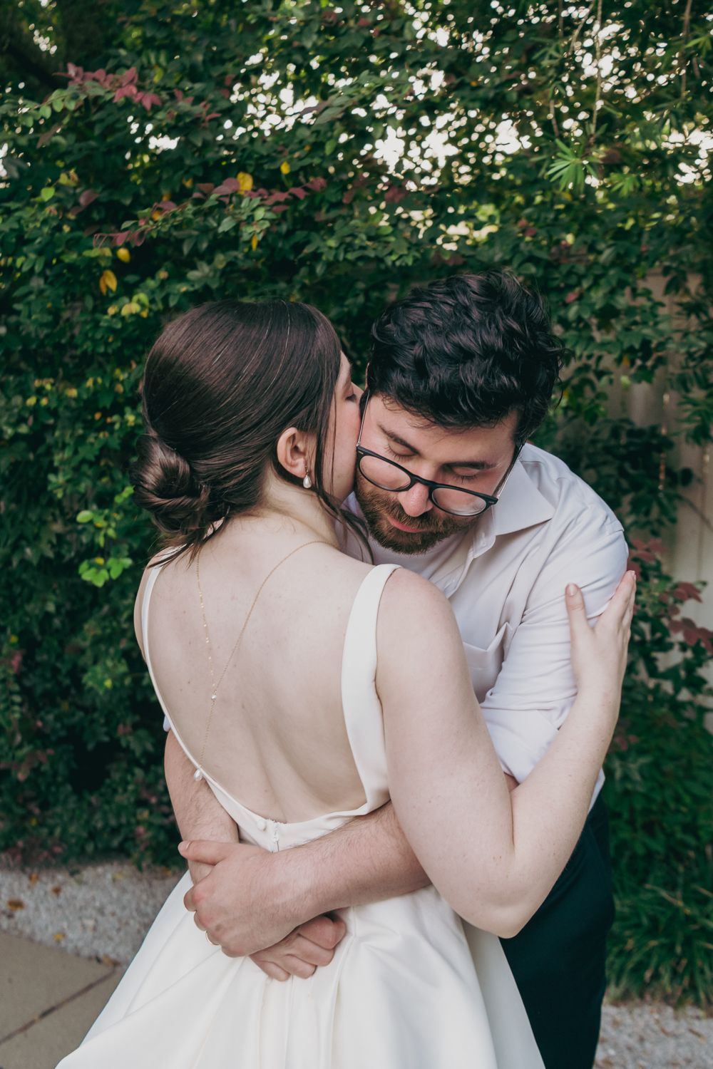 Bride and groom embrace tenderly in front of a lush green vine-covered wall during their wedding.