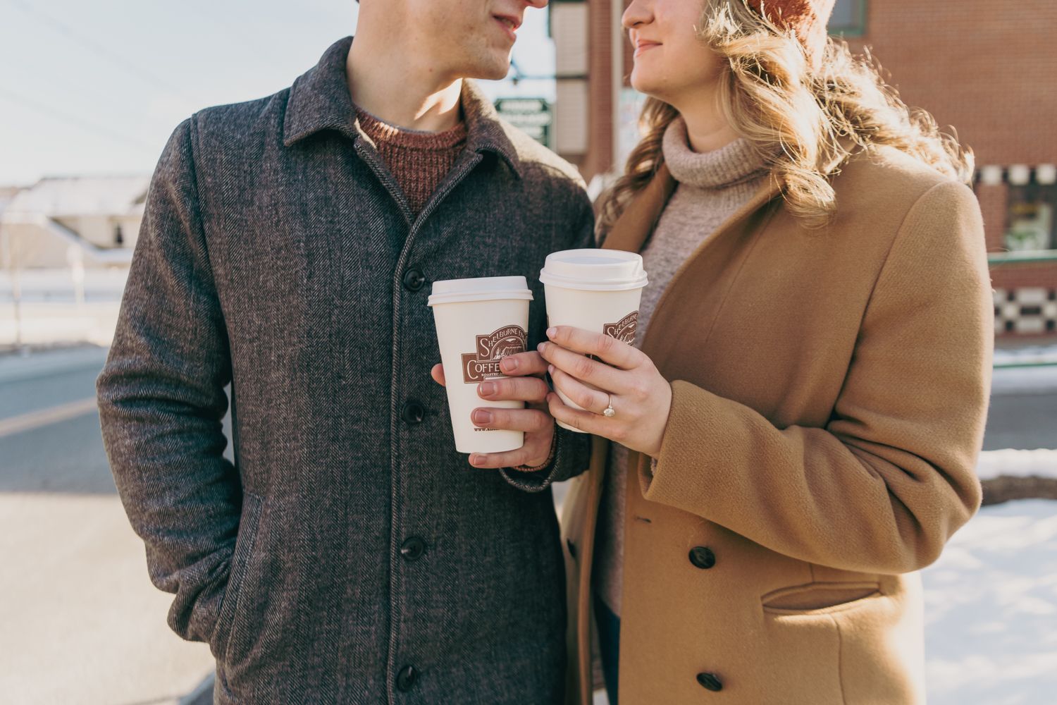Couple holding coffee cups together outdoors in winter, wearing cozy coats on a snowy day.