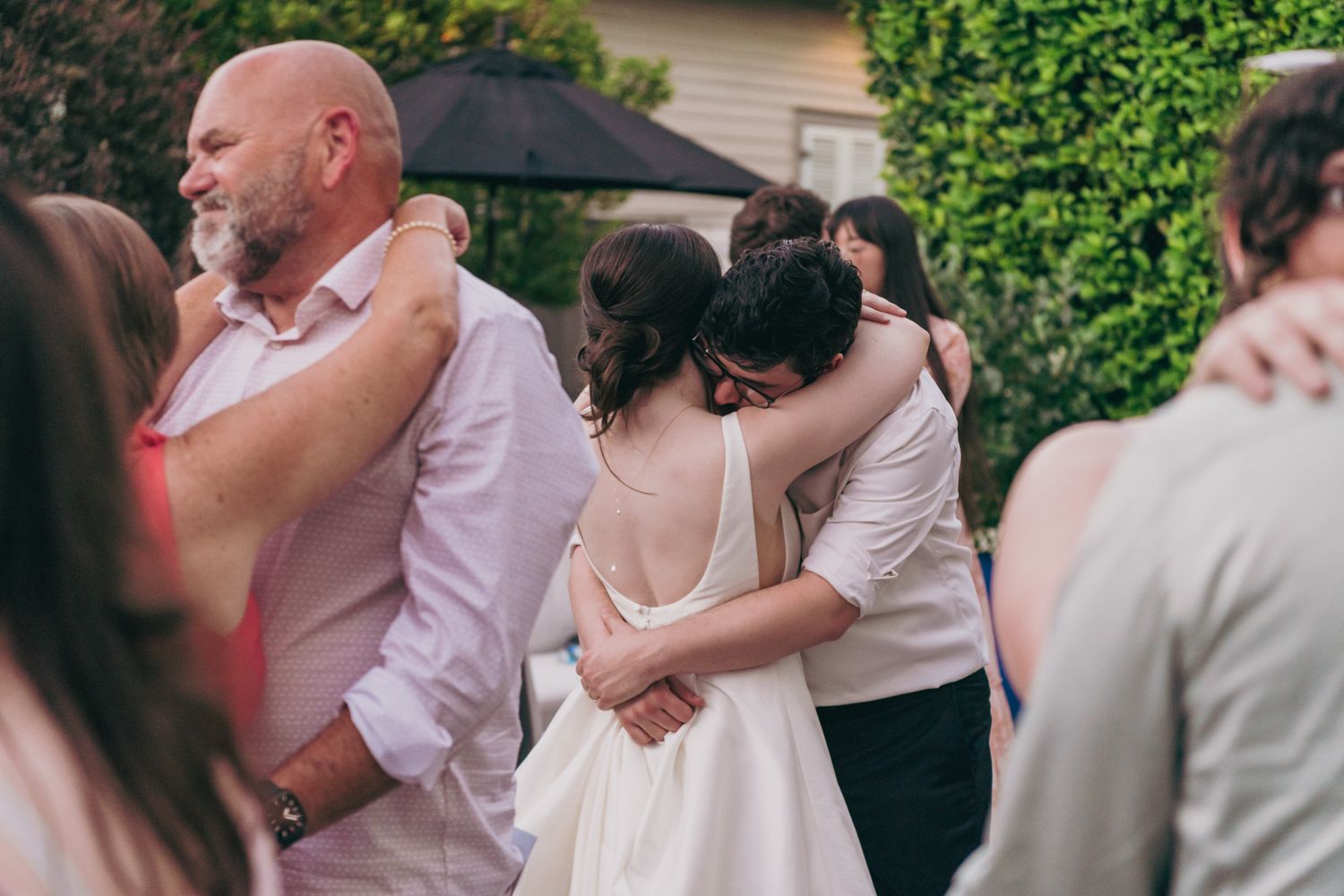 Bride hugs a guest warmly during an outdoor wedding reception surrounded by other dancing guests.