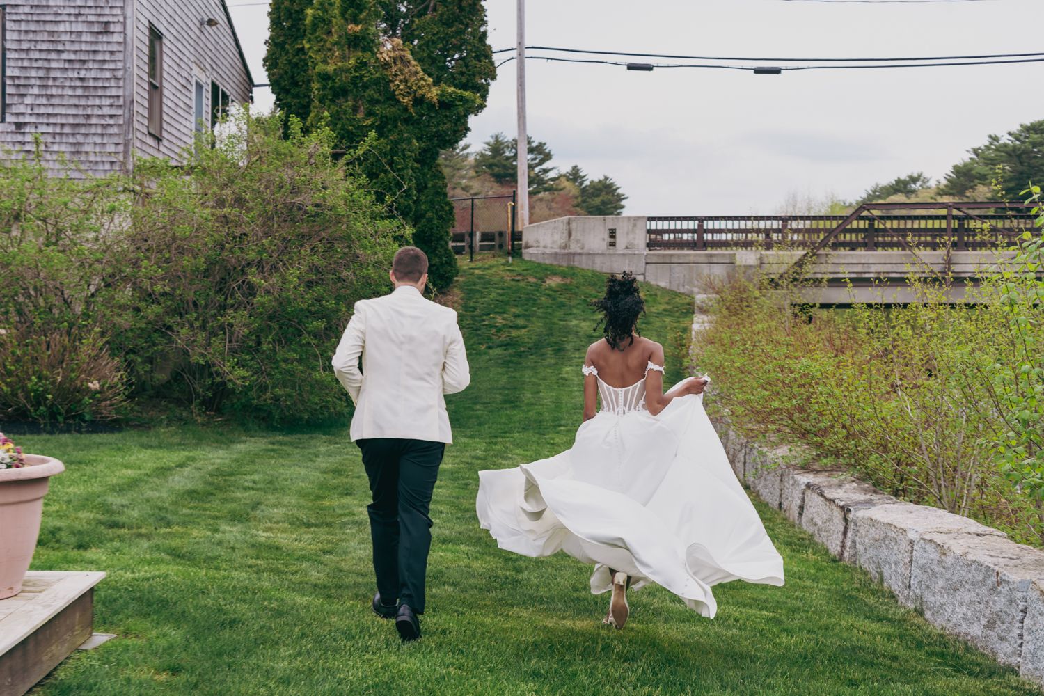 Bride and groom walking hand in hand across lush green lawn at outdoor wedding venue.