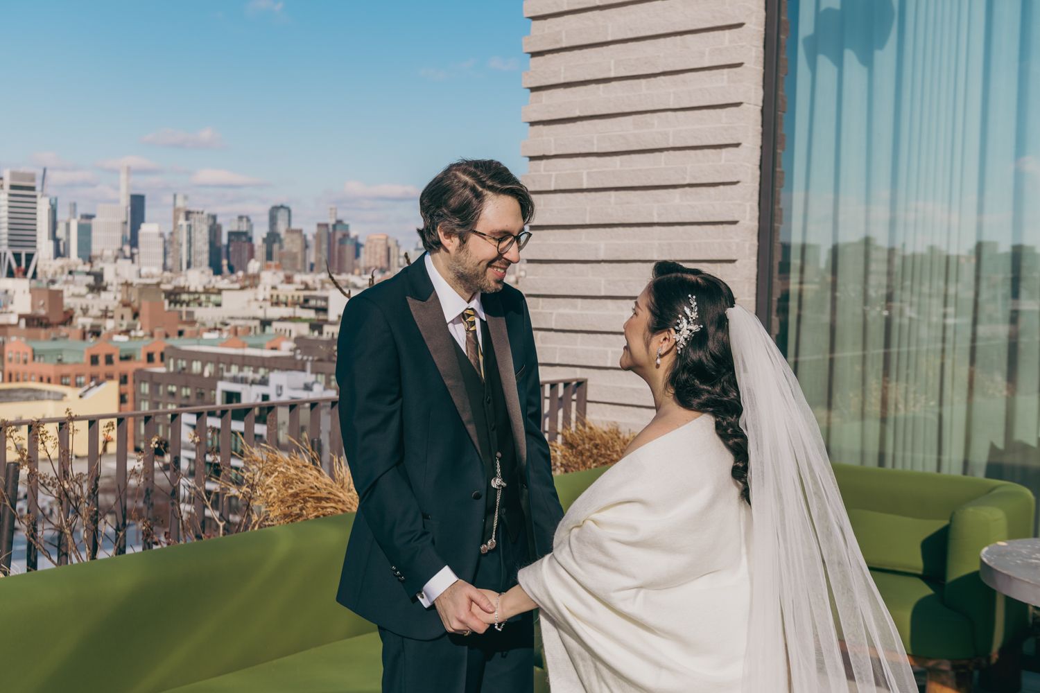 Bride and groom holding hands on rooftop with city skyline backdrop on wedding day.