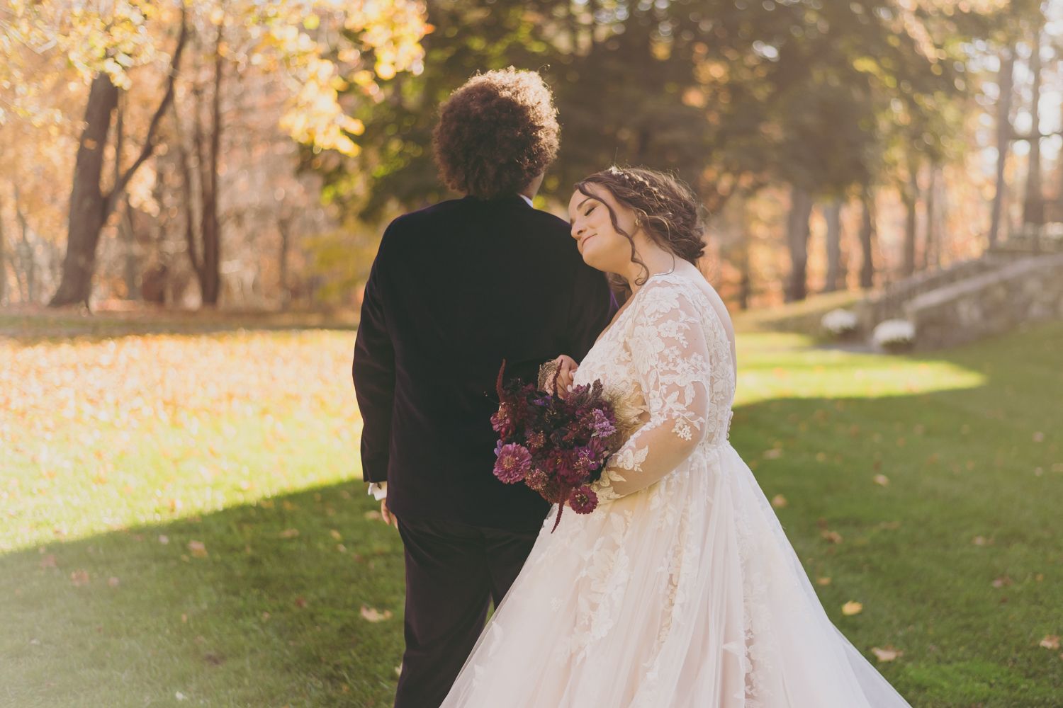 Bride and groom share romantic autumn moment on lawn surrounded by golden fall foliage.