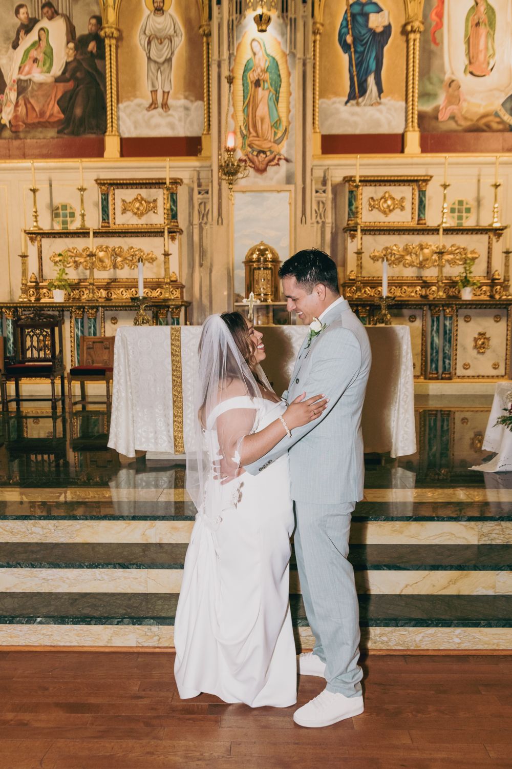 Bride and groom share a romantic moment at the altar of an ornate church with golden decor.