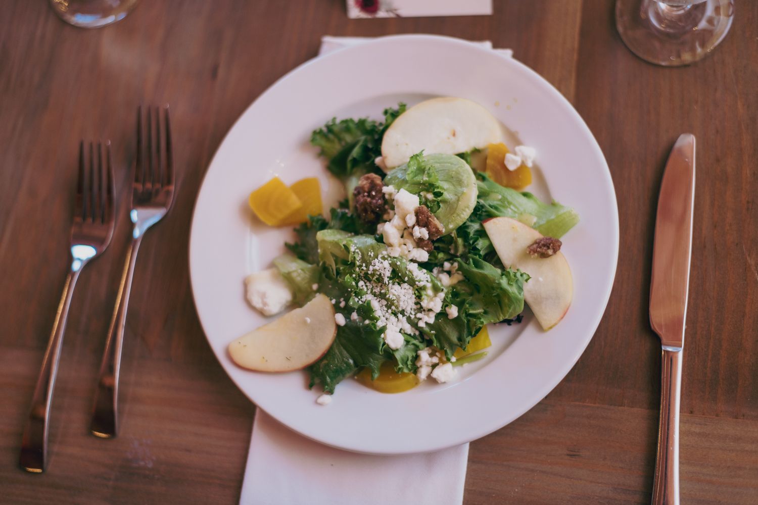 Fresh green salad with apples, feta, and walnuts on a white plate at a wedding reception.