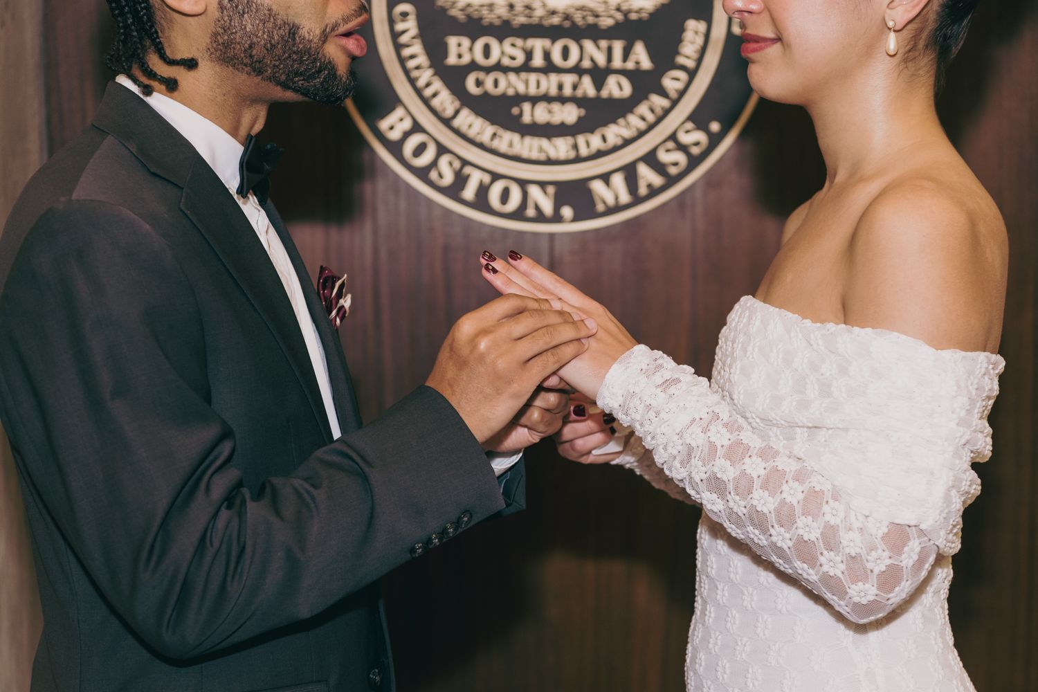 Couple exchanging rings during a wedding ceremony in front of the Boston, Mass. city seal.
