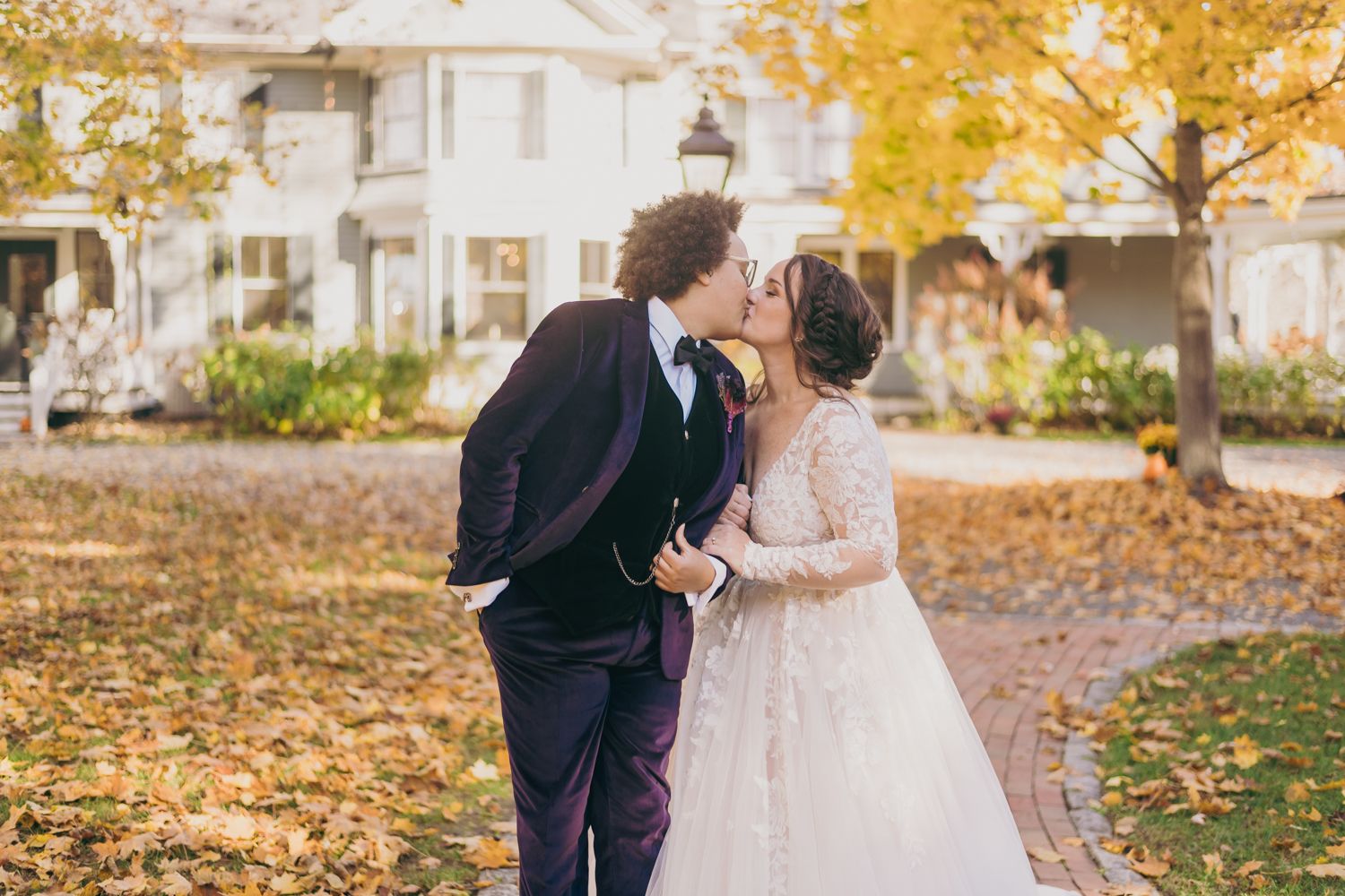 Newlyweds sharing a kiss outdoors surrounded by golden fall leaves.