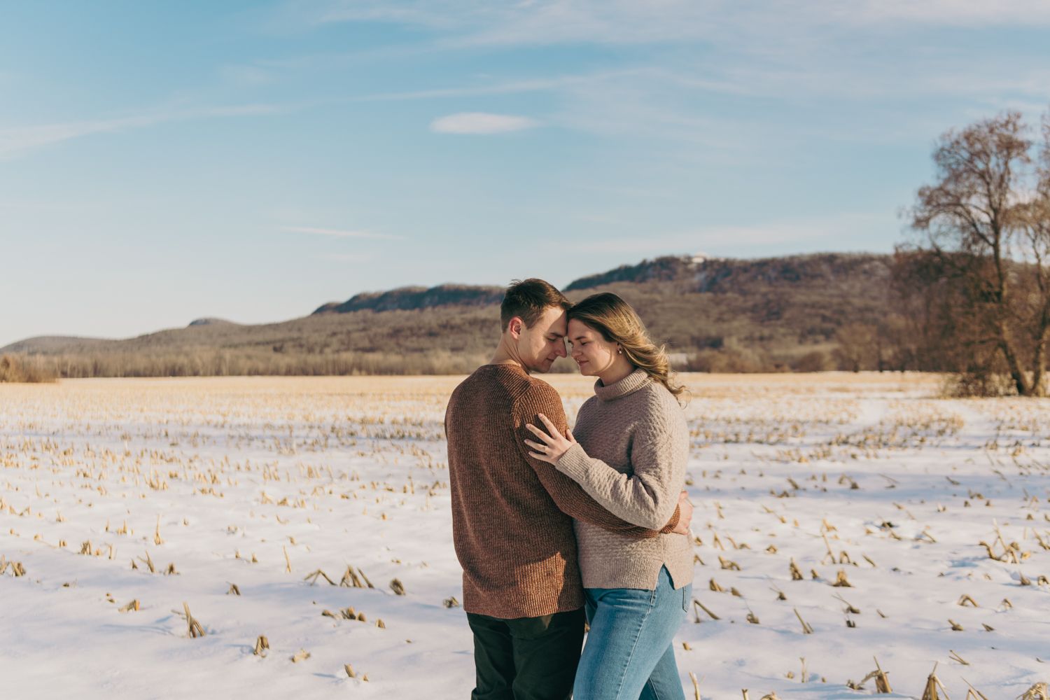 Romantic couple embracing in a snowy field under a blue sky on a sunny winter day.