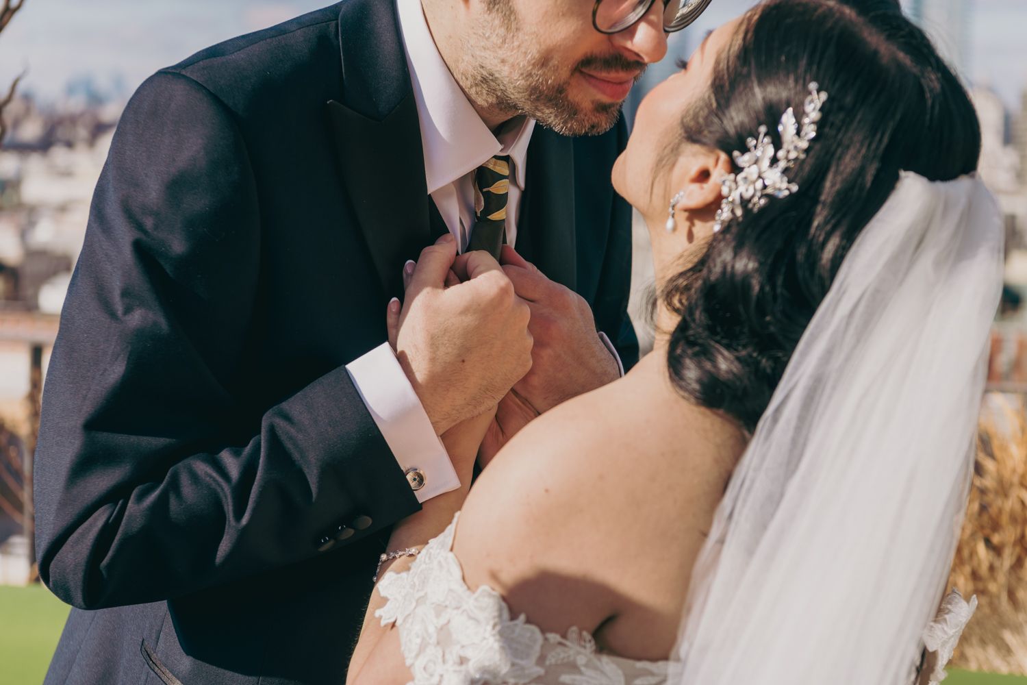 A bride and groom share an intimate moment, kissing closely as she holds his floral tie on their wedding day.