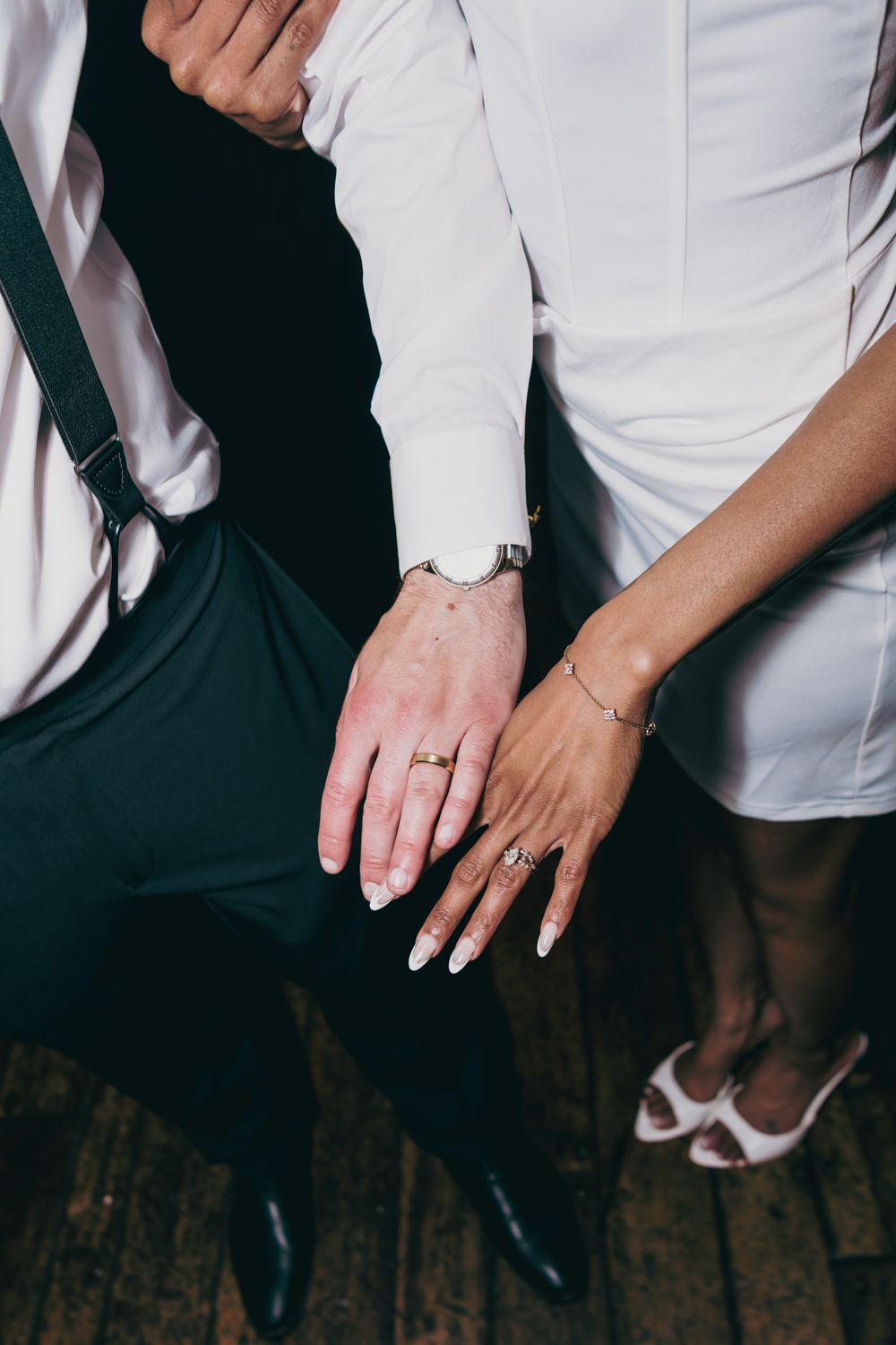 Close-up of newlyweds hands showing wedding rings and bracelets while seated together at wedding reception.