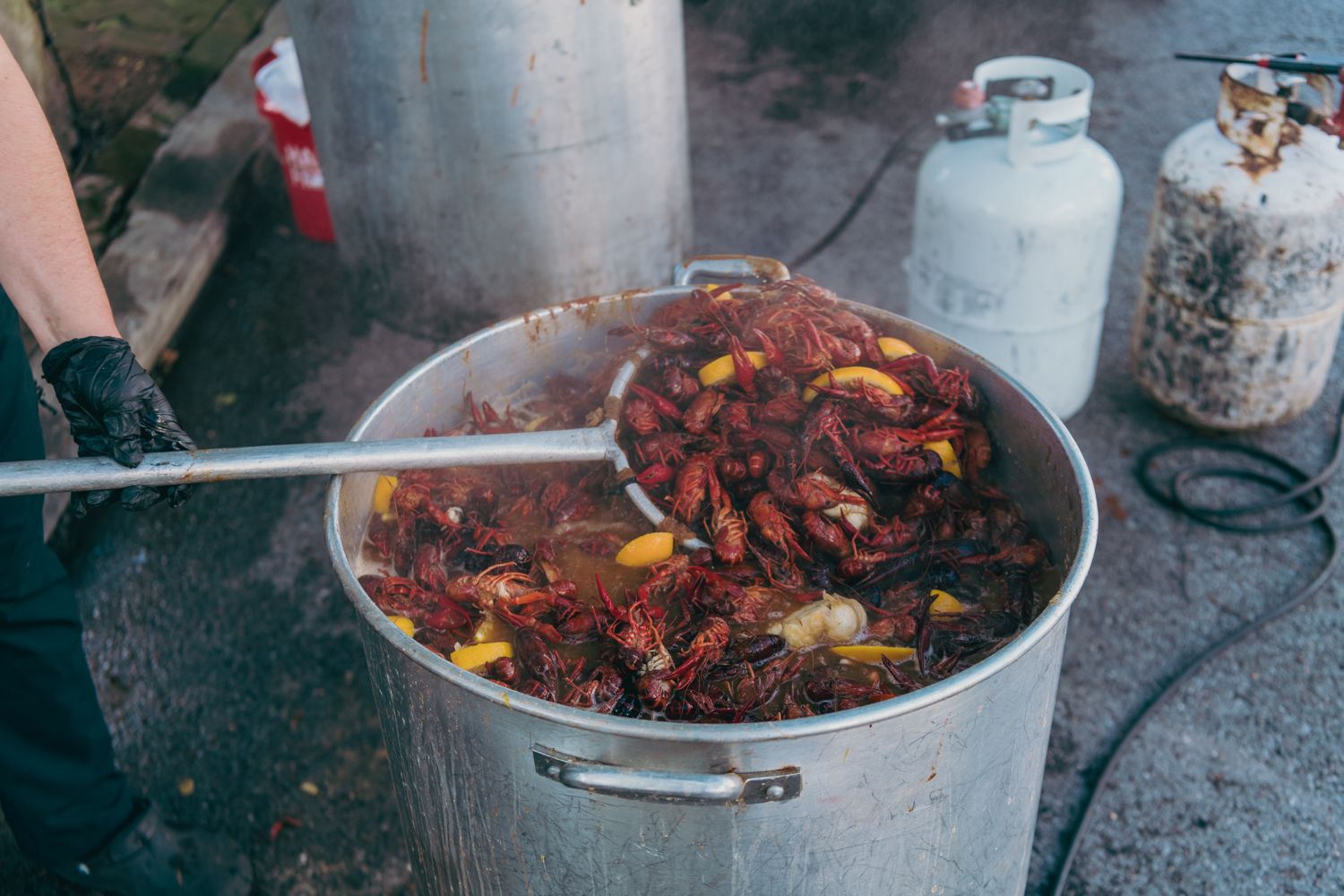 Large pot of steaming Cajun crawfish boil with corn and seasonings being stirred at an outdoor event.