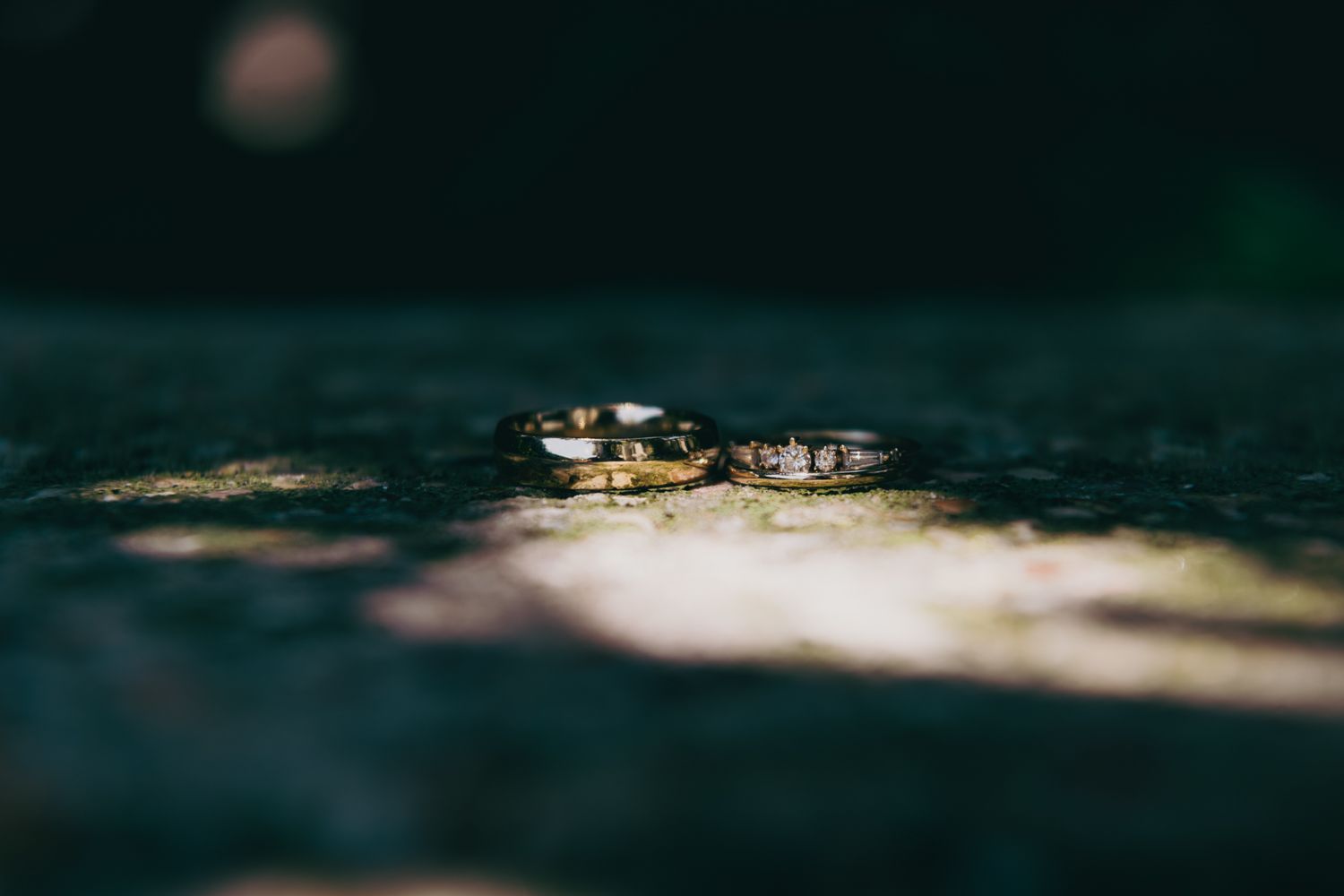 Two gold wedding bands resting on textured stone surface in dramatic lighting.