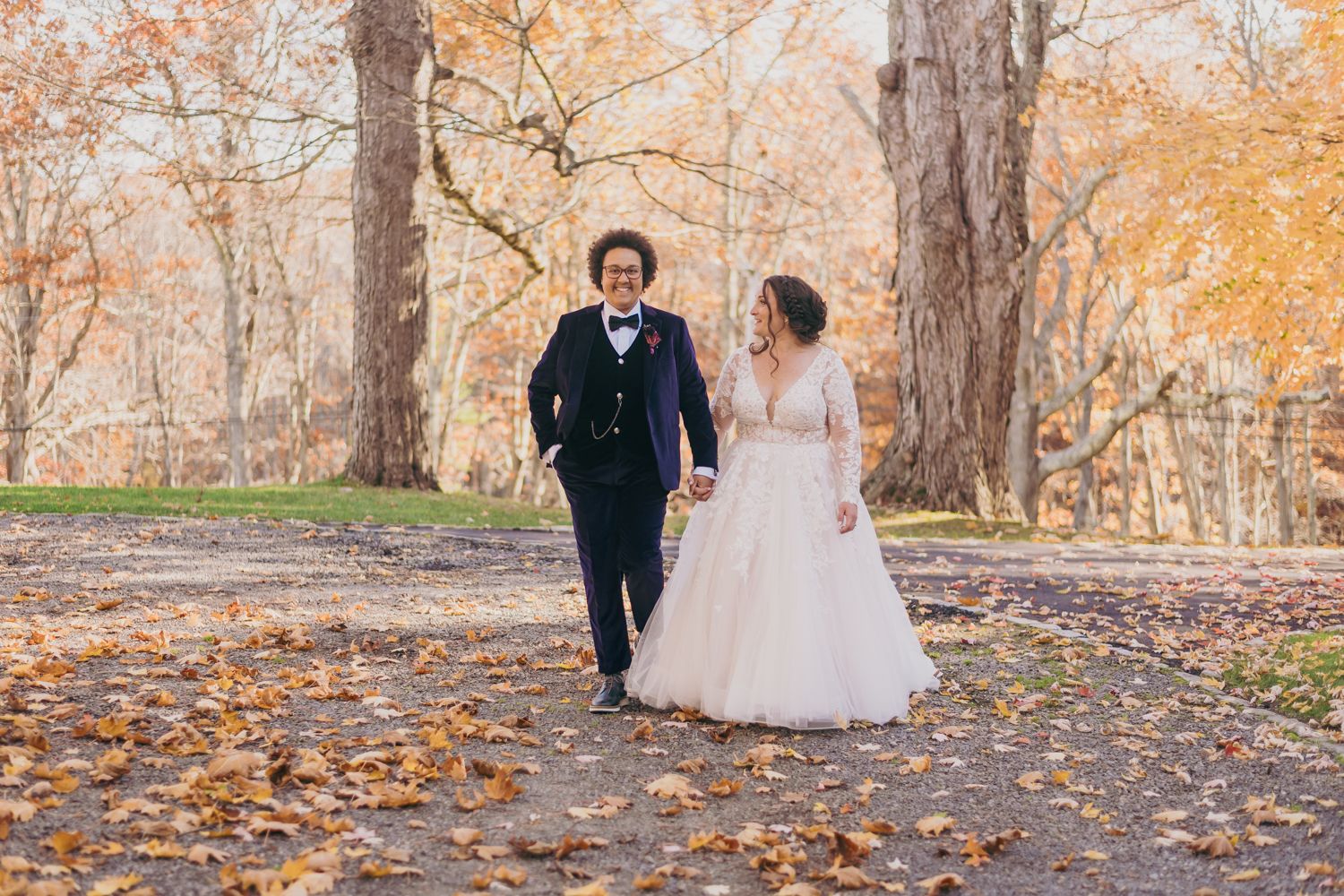 Bride and groom walking hand in hand through autumn park in wedding attire.