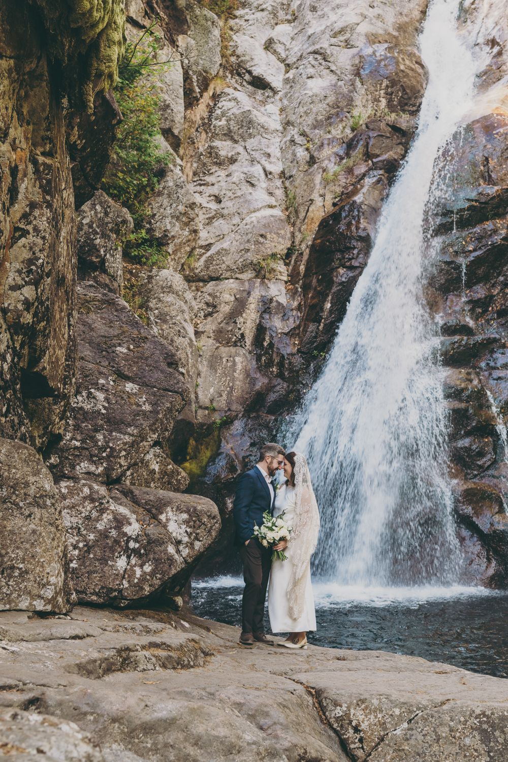 Couple shares a kiss in front of a dramatic waterfall on their wedding day.