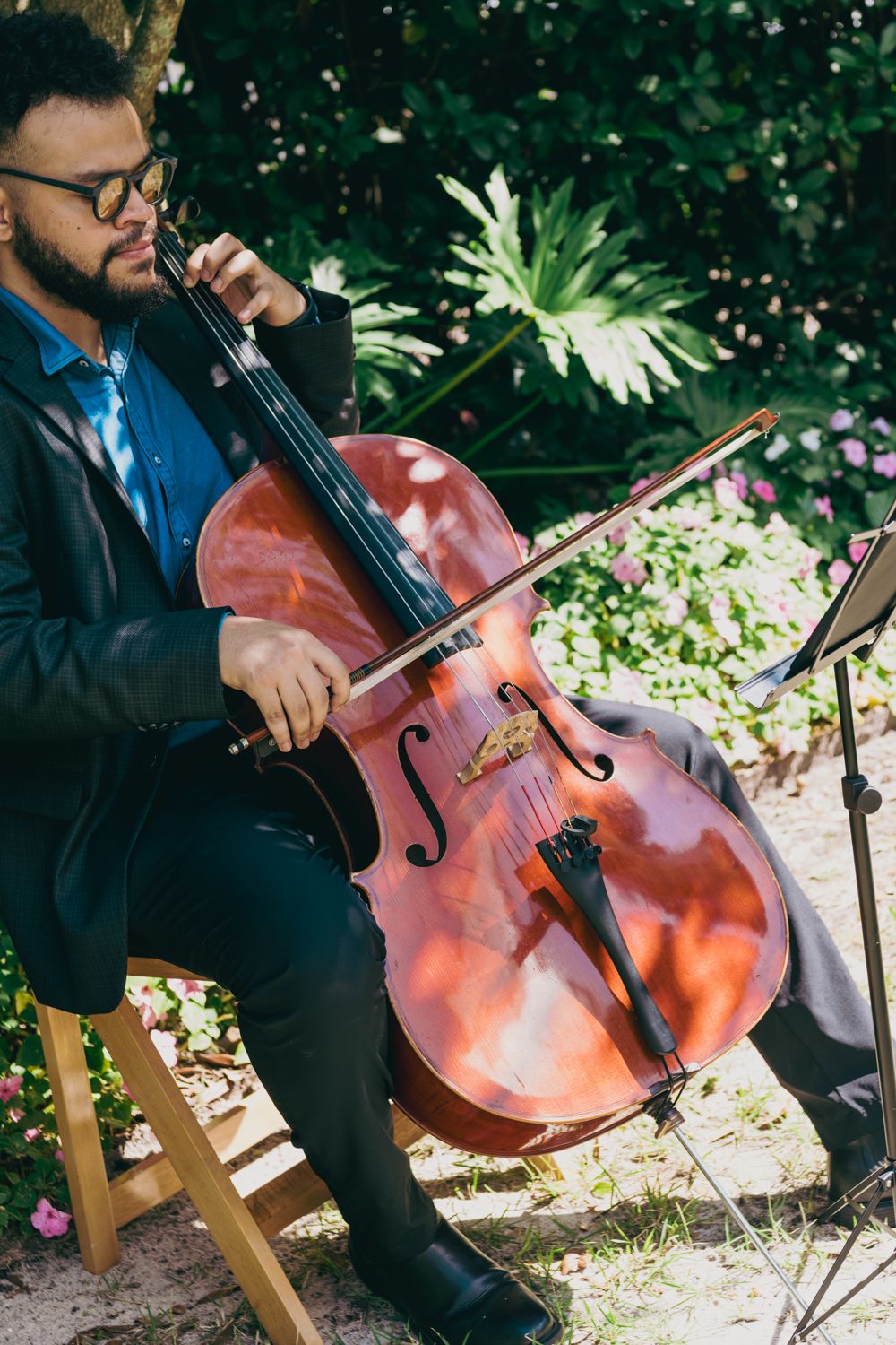Close-up of a cellist performing at an outdoor wedding ceremony surrounded by lush greenery.
