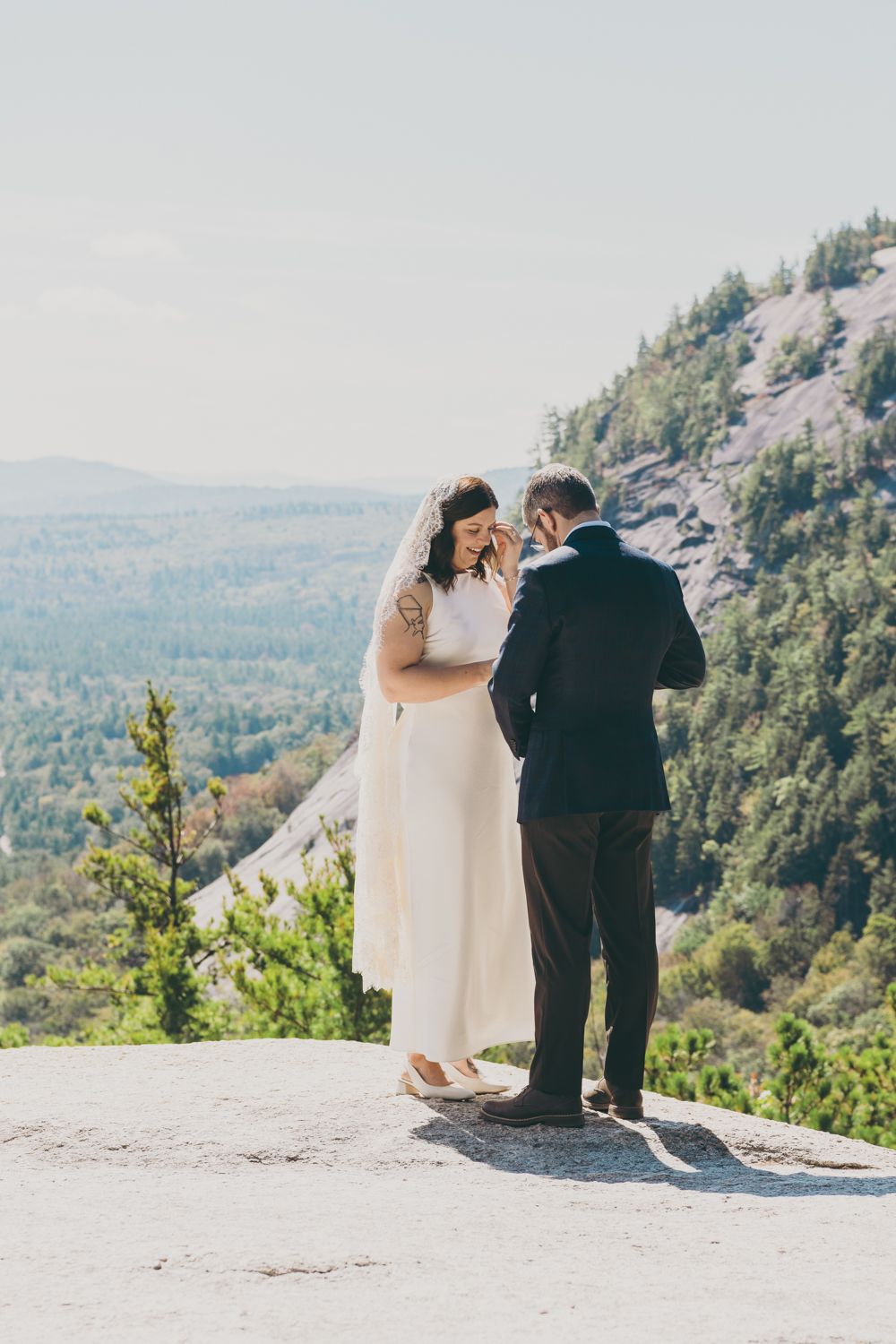 Bride laughing joyfully with groom during intimate outdoor mountain wedding ceremony on rocky summit.