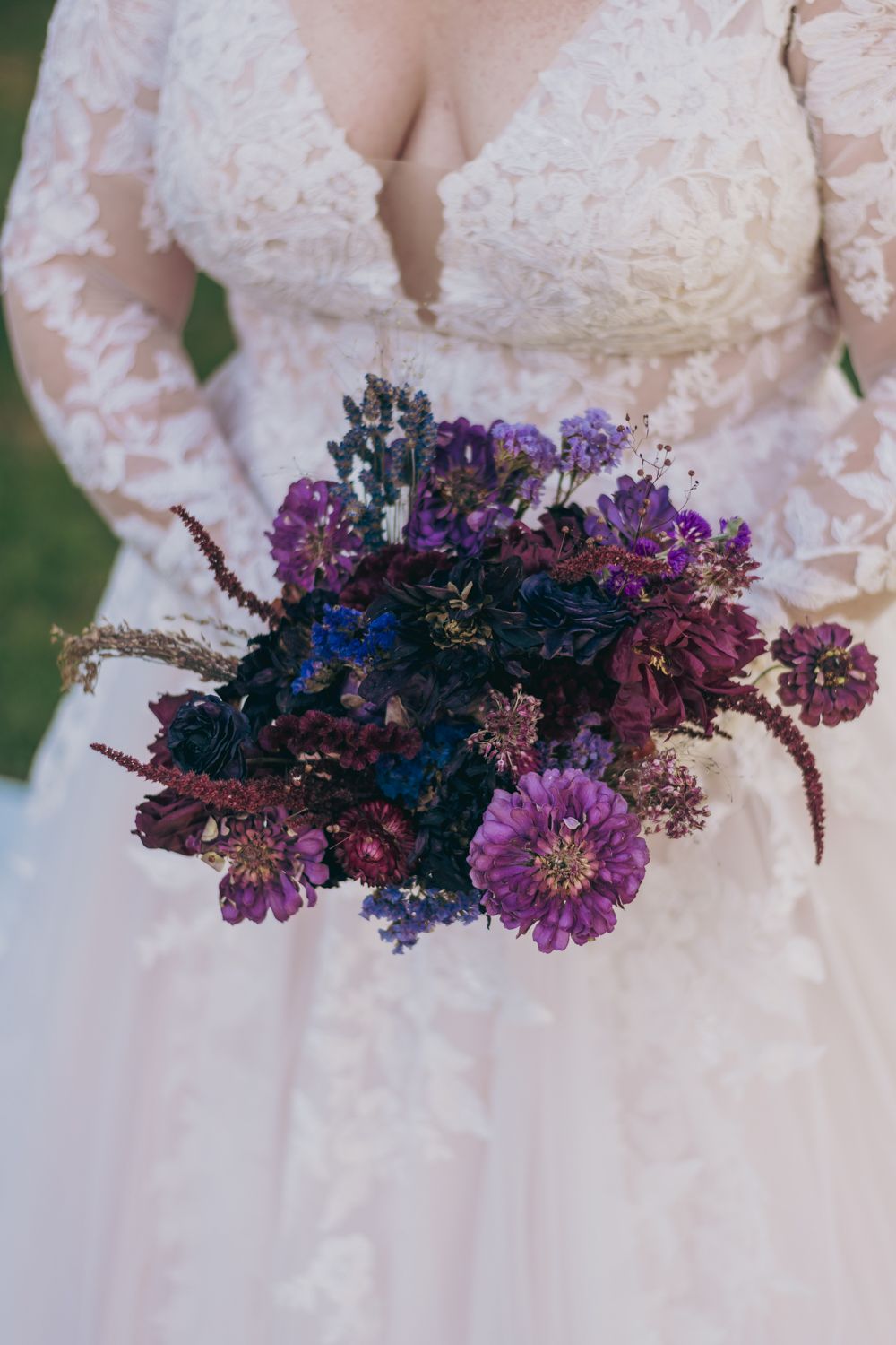 Bride in lace wedding gown holding stunning purple and burgundy wildflower bridal bouquet.
