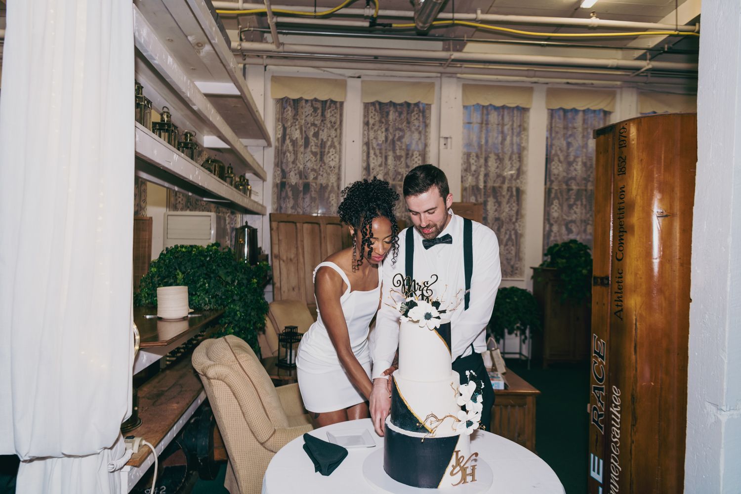 Interracial couple cutting their black and white wedding cake at indoor reception.