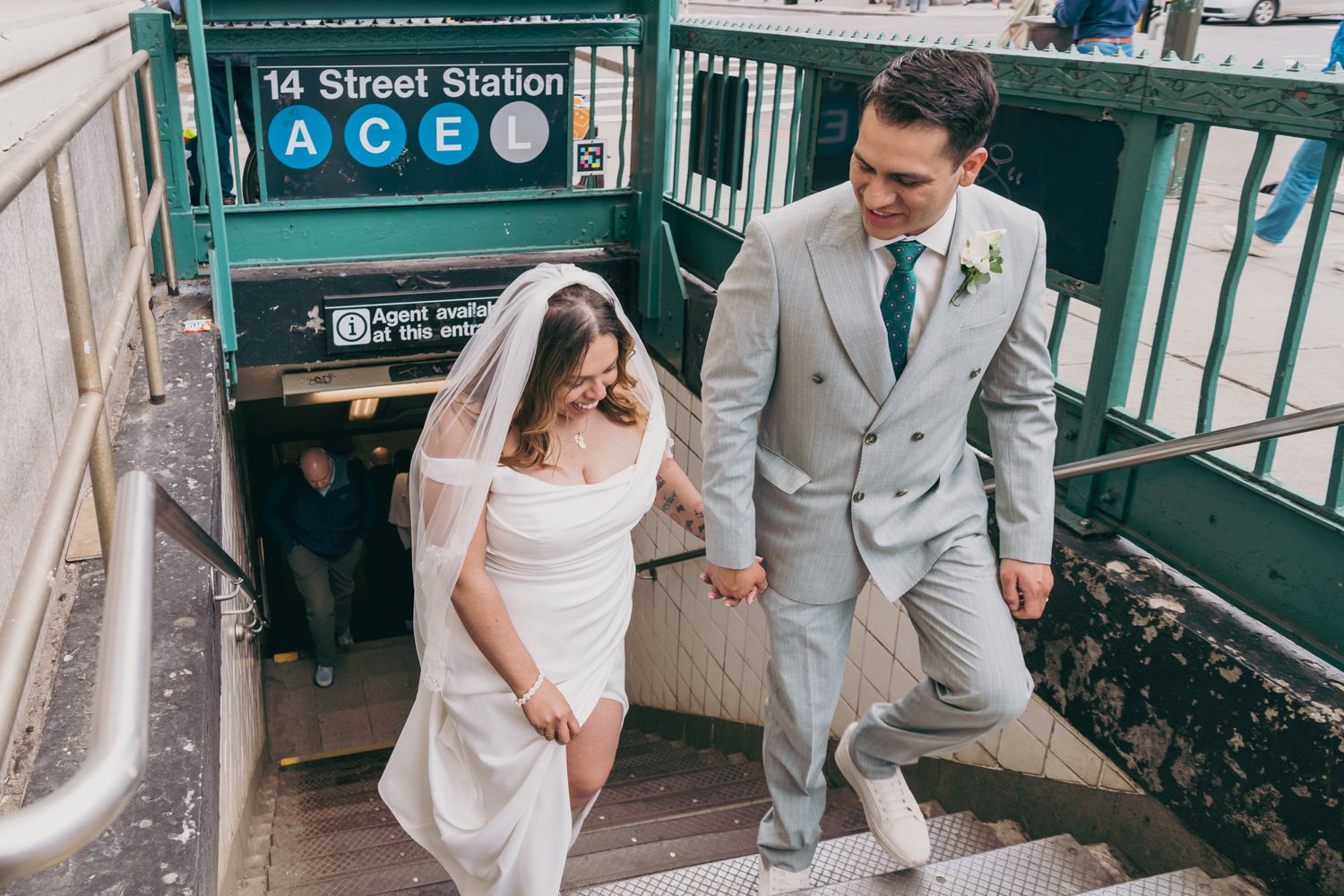 Bride and groom in wedding attire ascending NYC 14th Street subway station stairs.