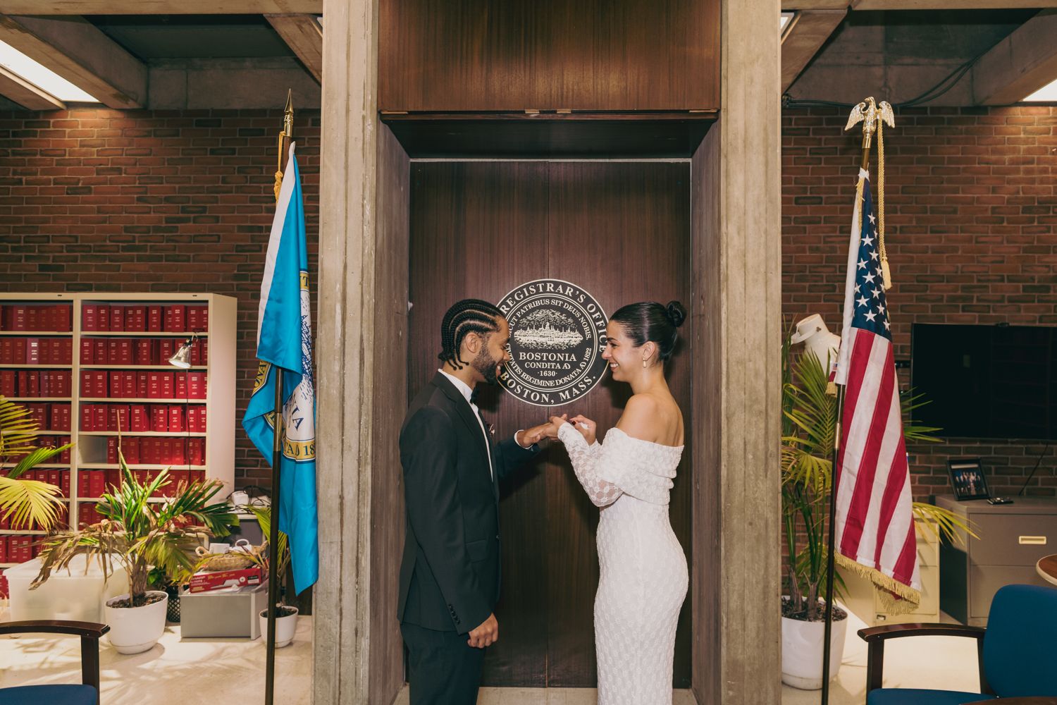Couple holds hands in elegant city hall wedding ceremony with American flag and official seal backdrop.
