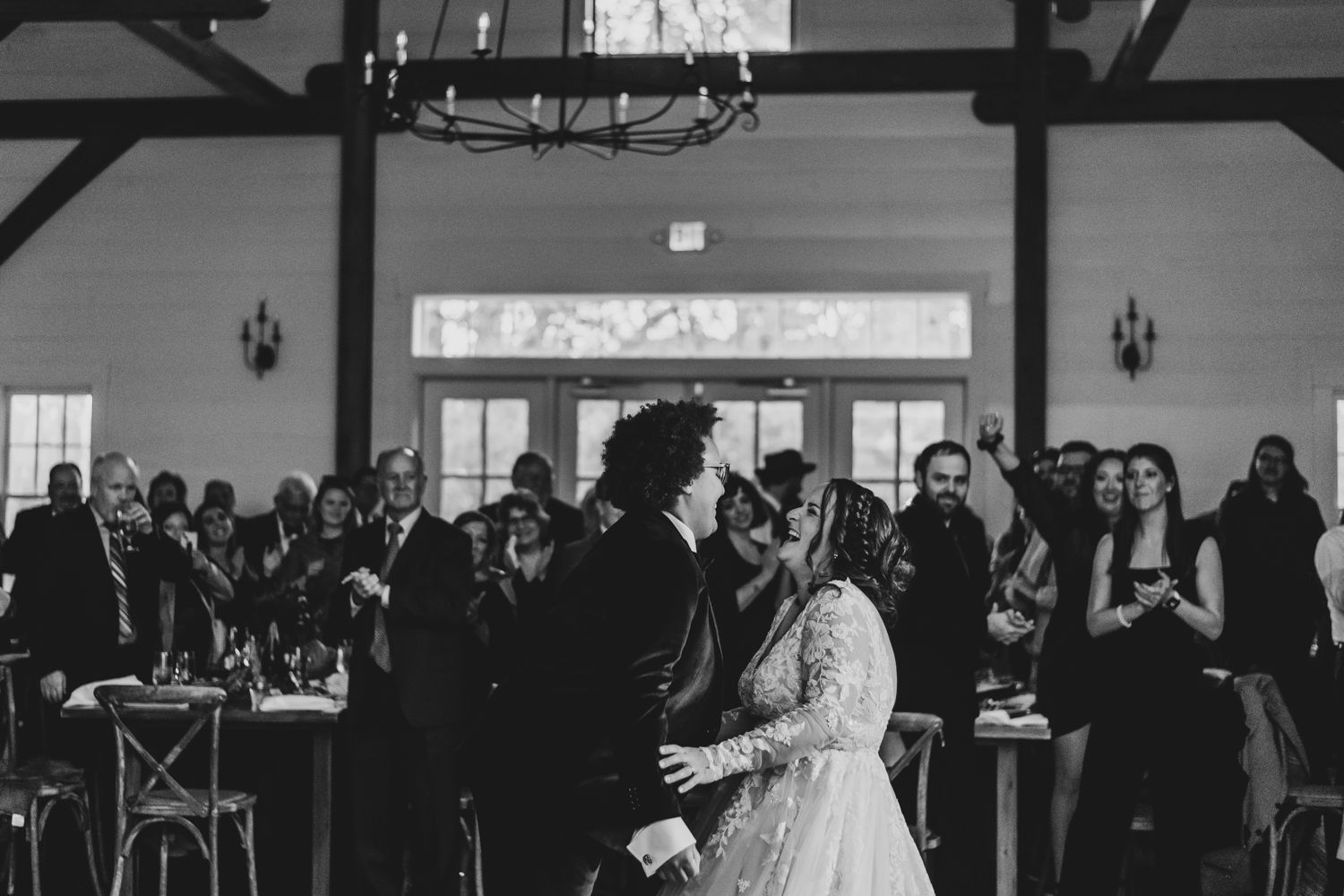 Black and white photo of newlyweds sharing their first dance in a rustic white barn reception venue.