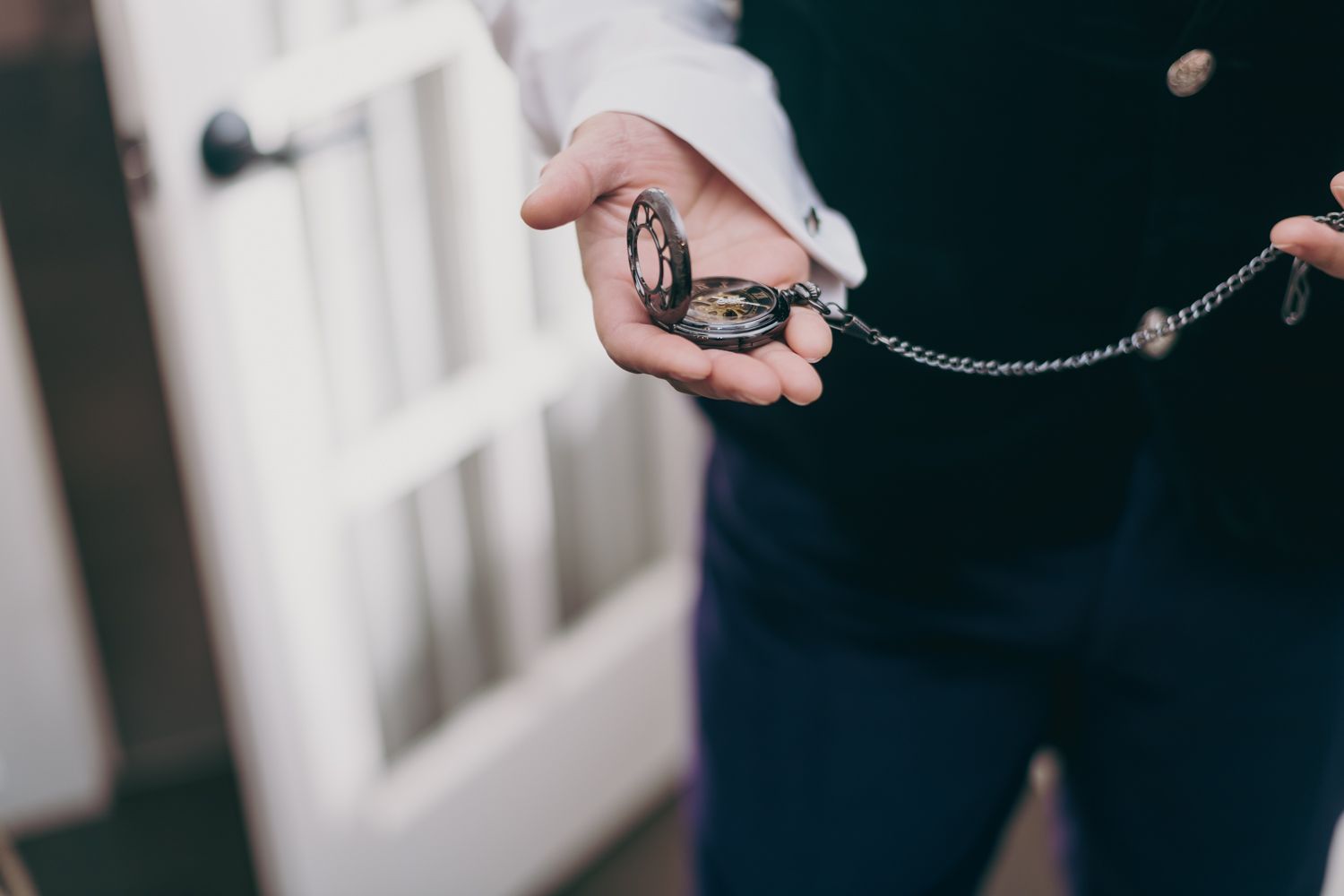 Groom holding a vintage silver pocket watch with chain on his wedding day.