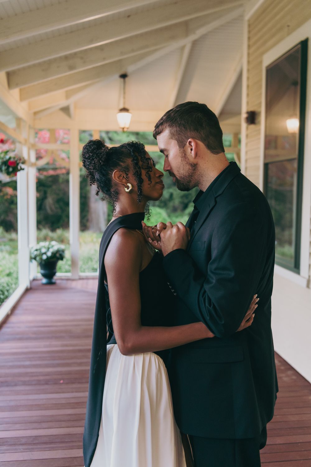 Interracial couple in elegant attire sharing a romantic moment on a wooden porch.