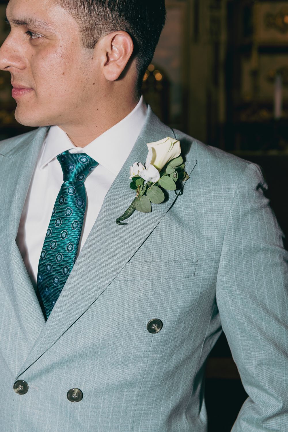 Close-up of groom in light gray pinstripe double-breasted suit with teal tie and white rose boutonniere.