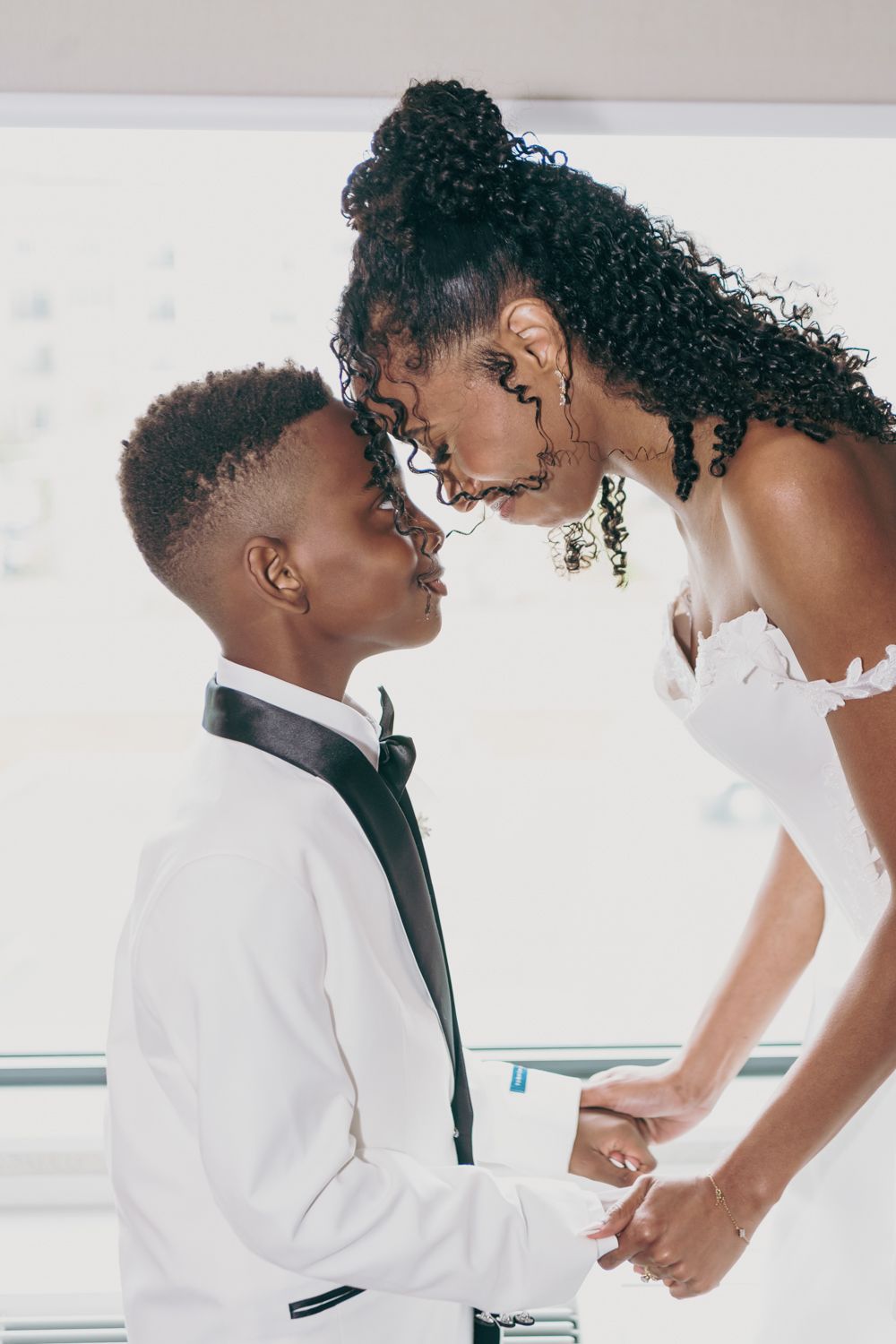 Black couple in wedding attire sharing an intimate moment, groom in white suit holding bride's hands.