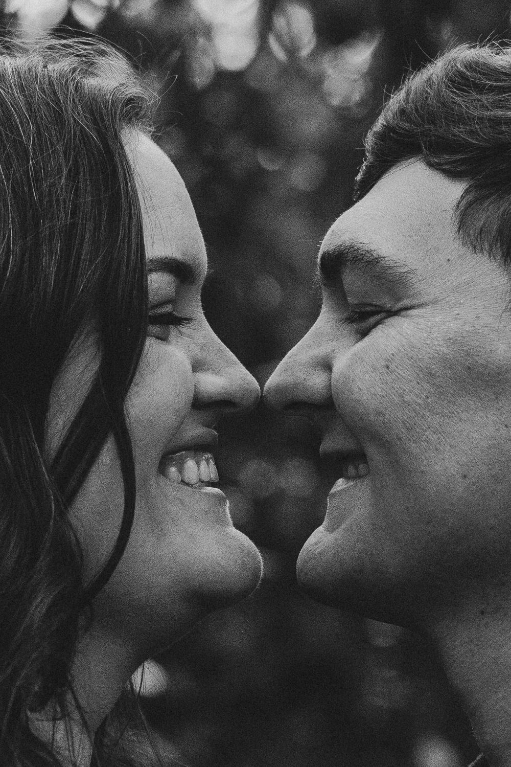Black and white close-up of a smiling couple facing each other, noses almost touching, sharing a romantic moment.