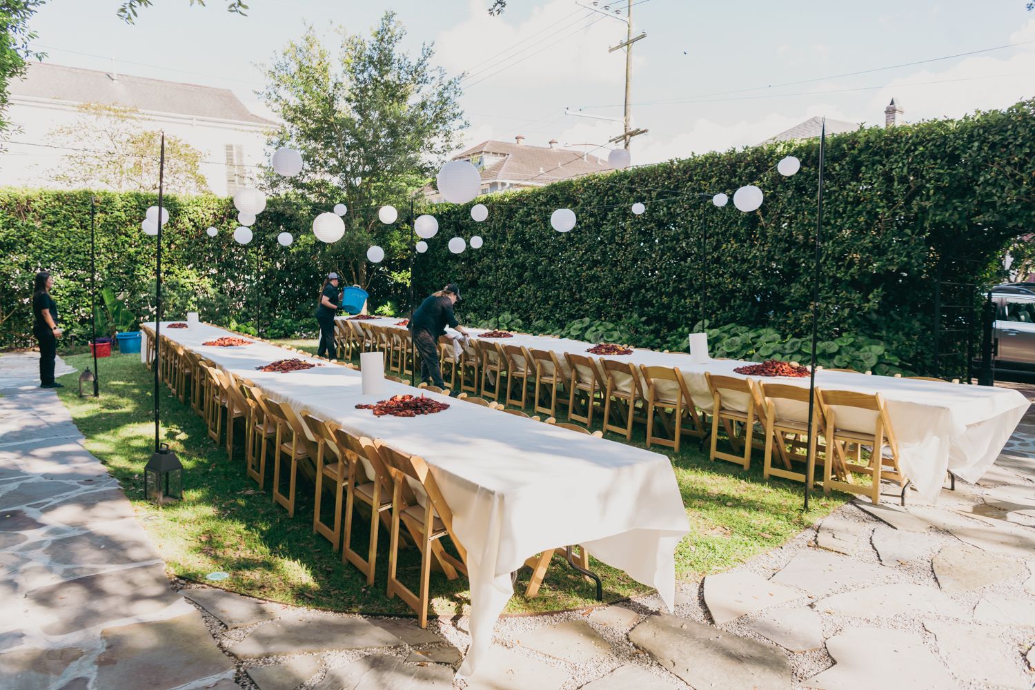 Outdoor wedding reception with long white-clothed tables, wooden chairs, and paper lanterns in a garden setting.