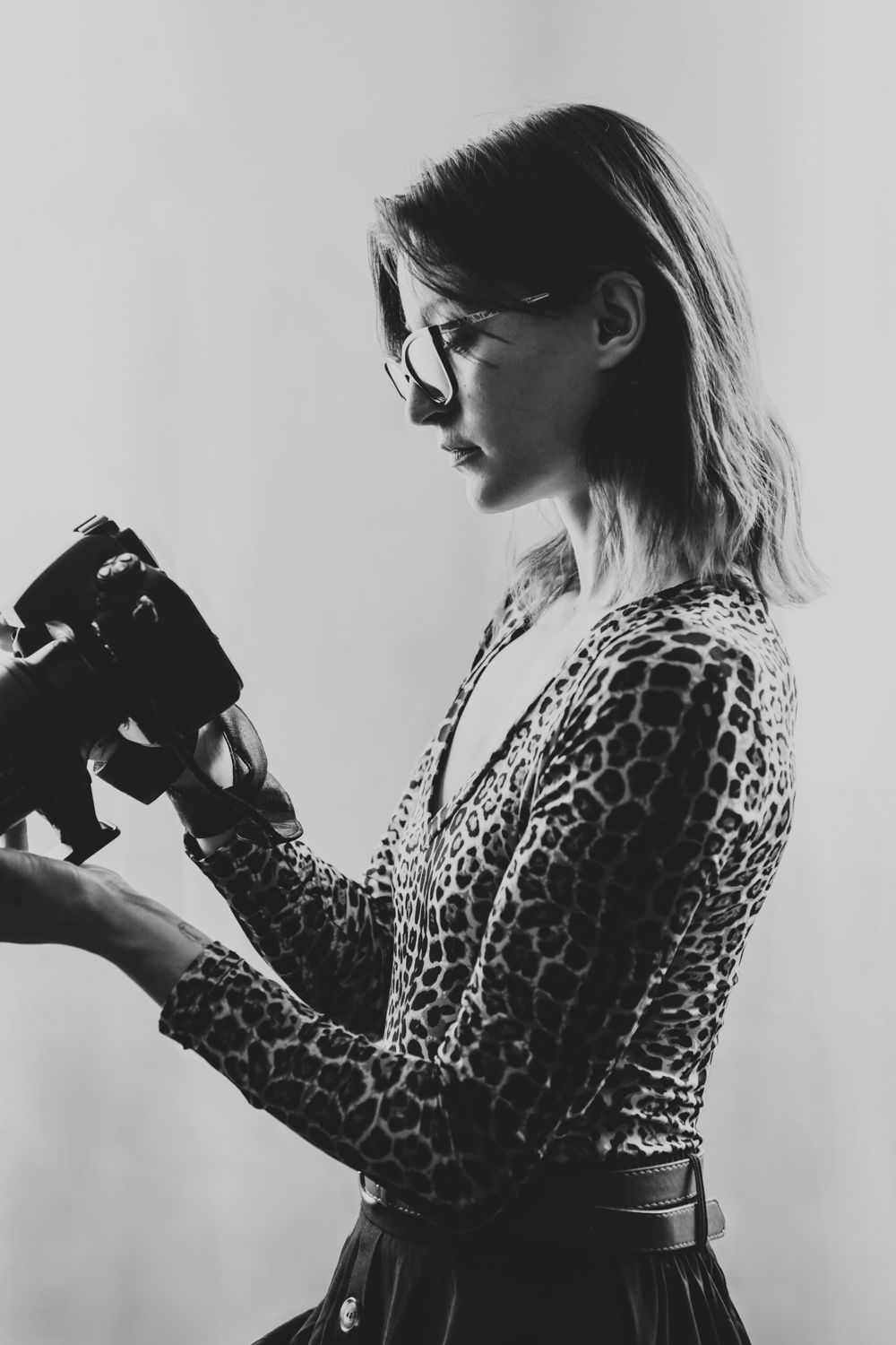 Black and white portrait of blonde female photographer in leopard print top holding camera.