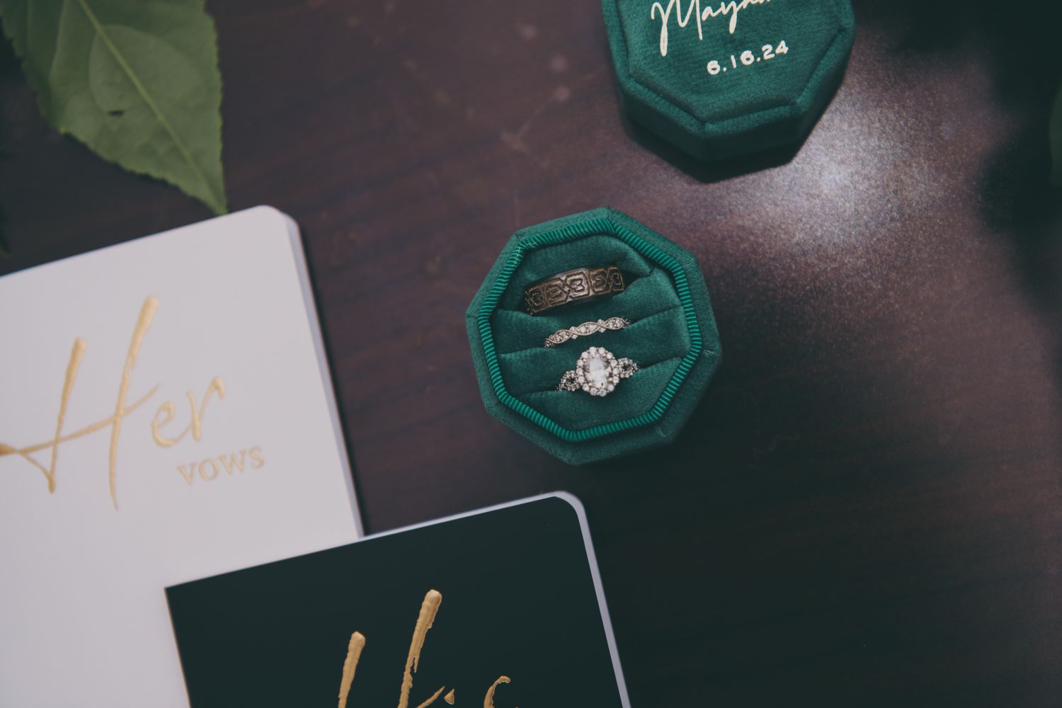 Wedding rings displayed in green velvet octagonal ring box alongside His and Her vow books.