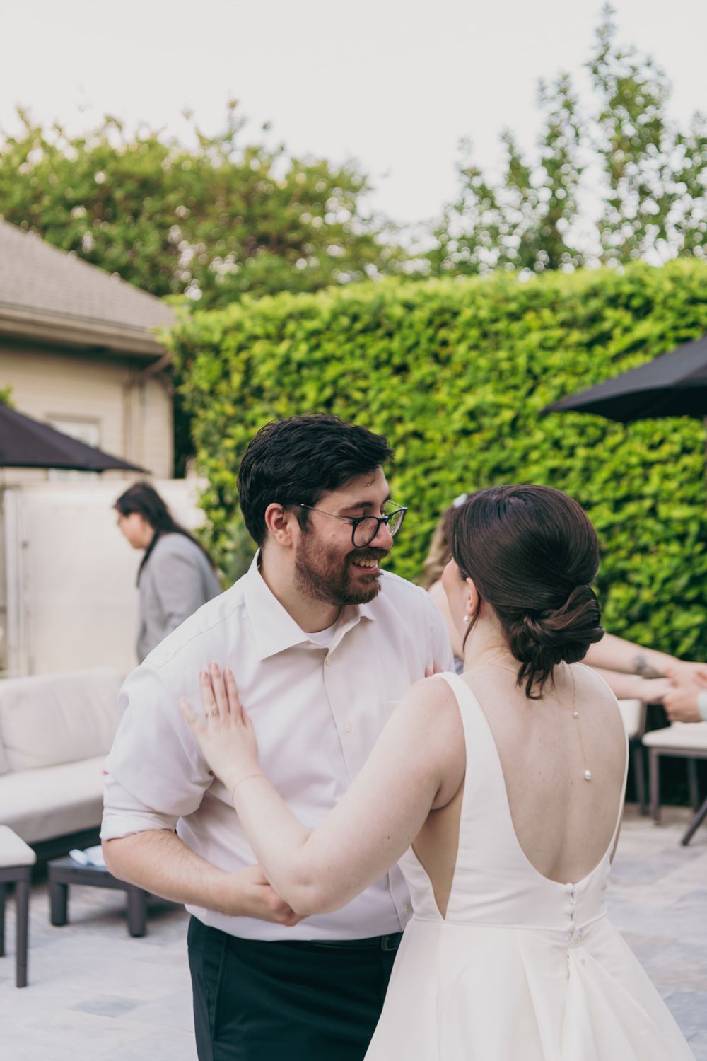 Bride and groom share a joyful first dance outdoors at their wedding reception surrounded by lush green hedges.