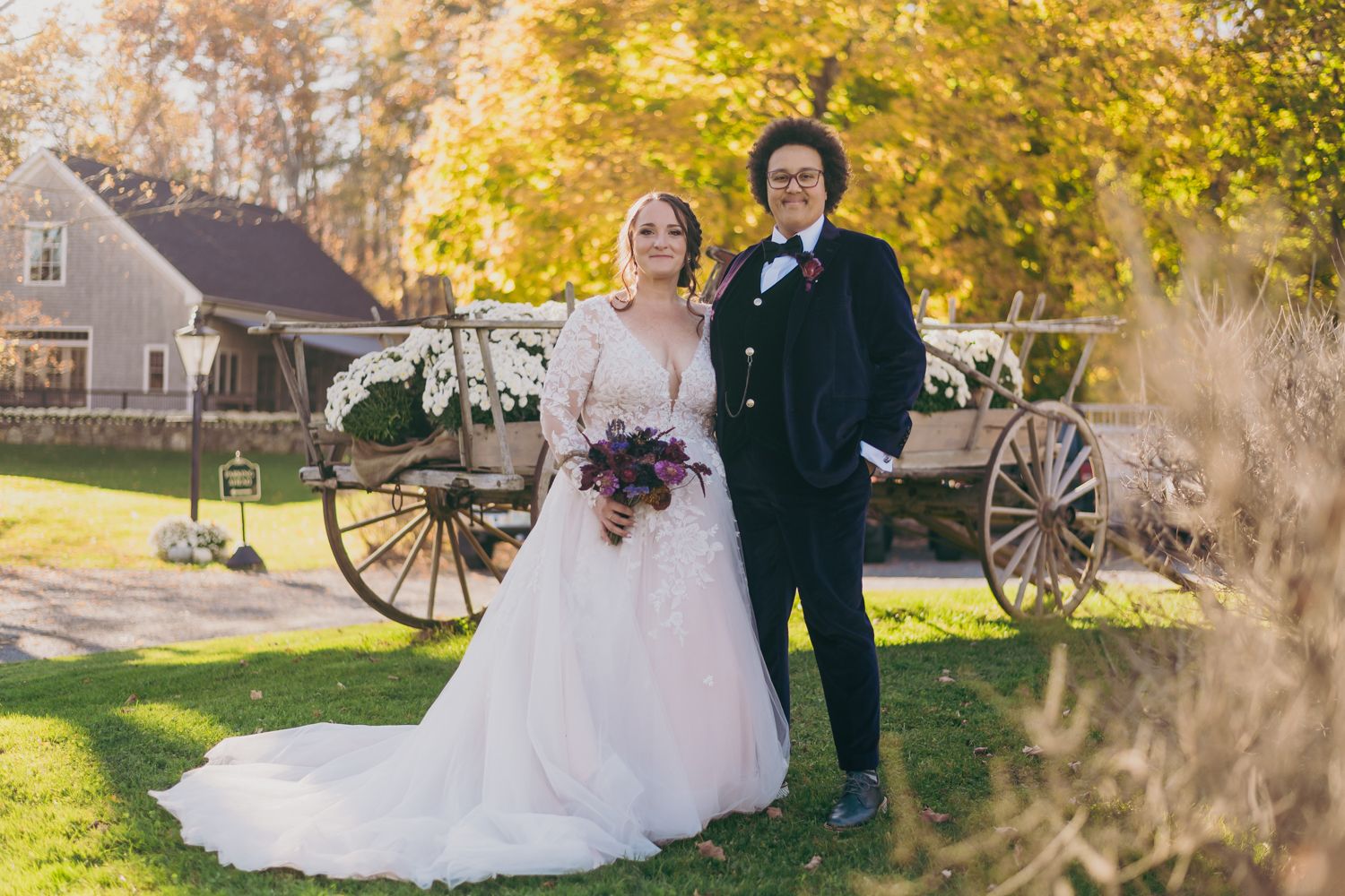 Bride and groom posing before rustic wagon in vibrant autumn outdoor wedding setting.