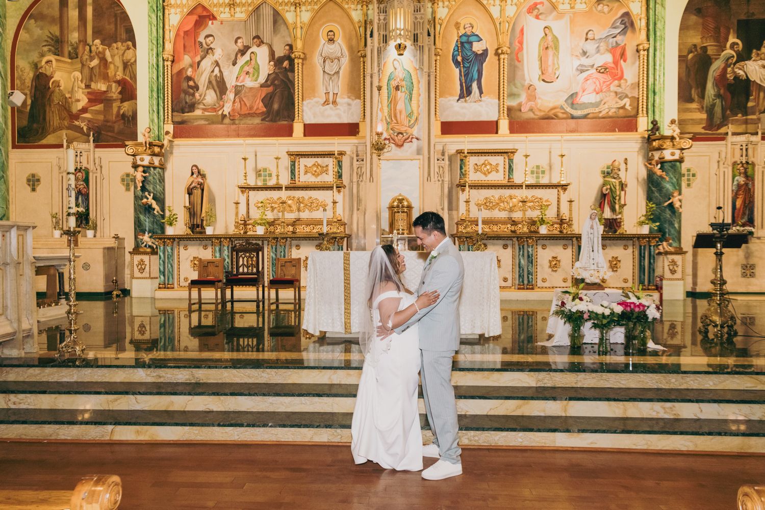 Bride and groom sharing a romantic embrace at the altar of a beautifully decorated Catholic church.