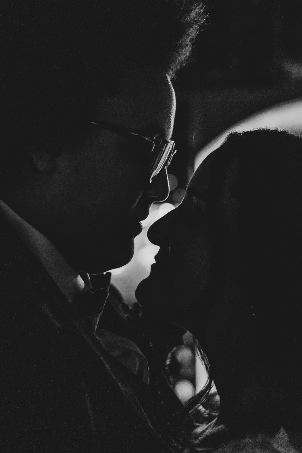 Romantic black and white silhouette of couple nearly kissing with glasses detail visible.