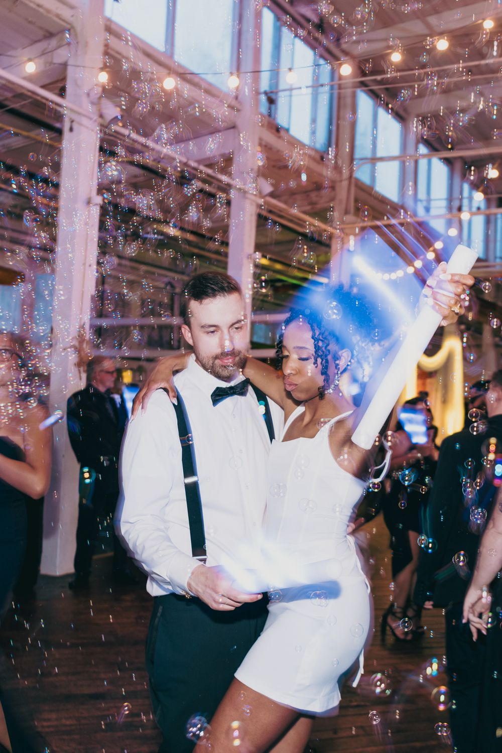 Newlyweds share first dance surrounded by bubbles at lively wedding reception.
