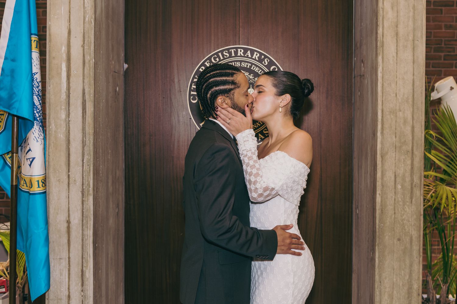 Couple sharing a first kiss as newlyweds outside a registrar office door on their wedding day.