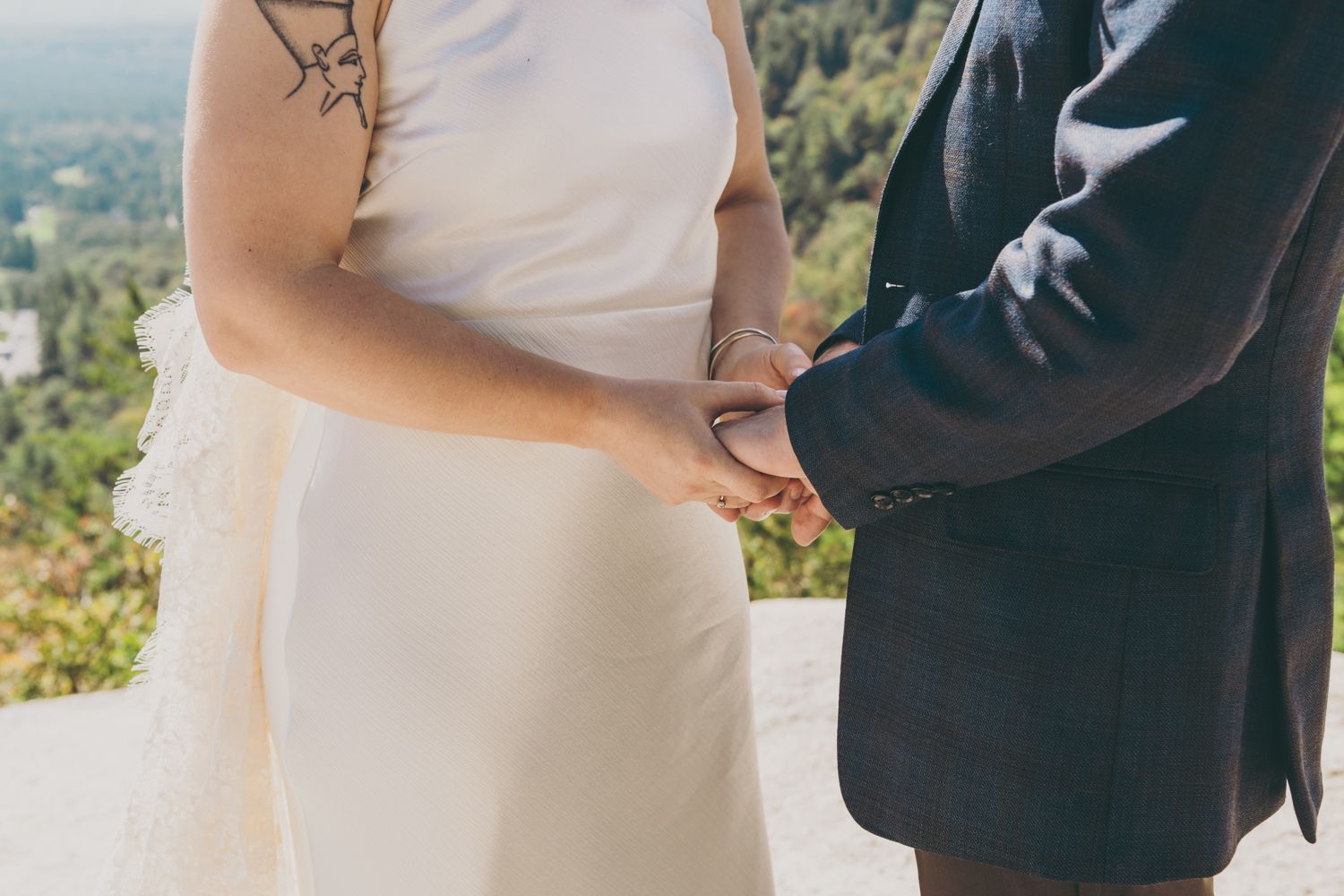 Close-up of bride and groom holding hands during outdoor mountain wedding ceremony.