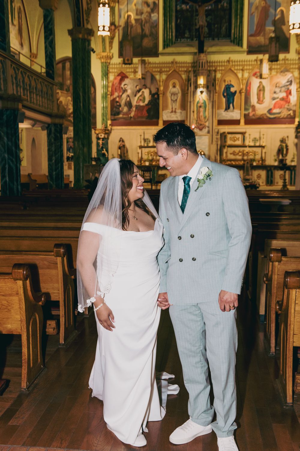 Bride and groom share a joyful moment in a ornate Catholic church aisle after their wedding ceremony.