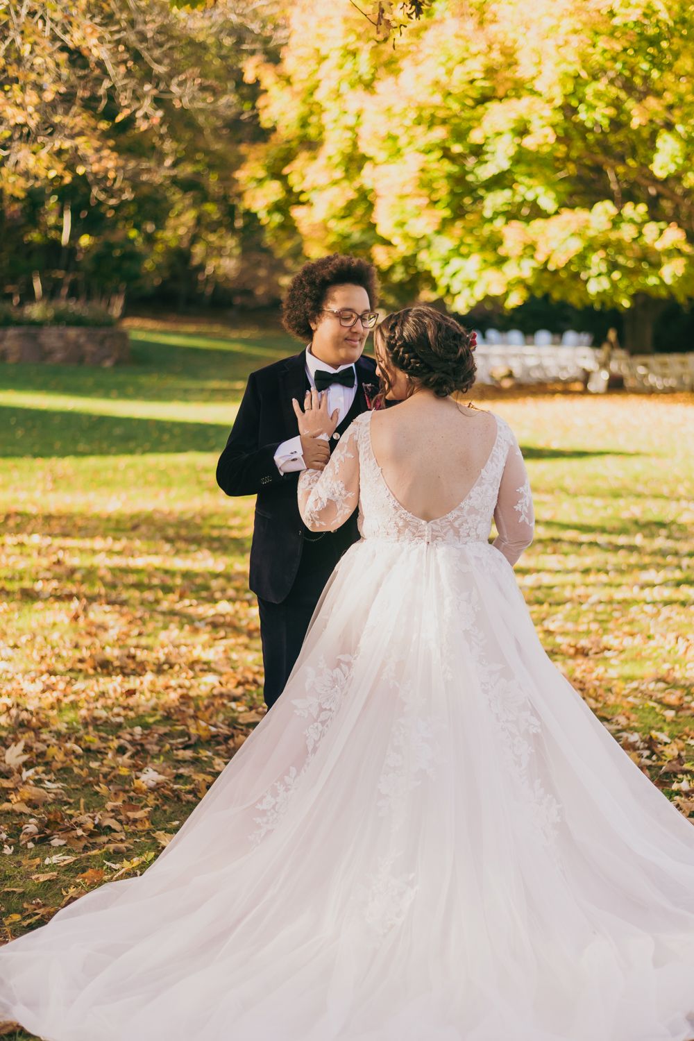 Bride in lace ball gown with low back and groom in tuxedo sharing romantic moment outdoors.