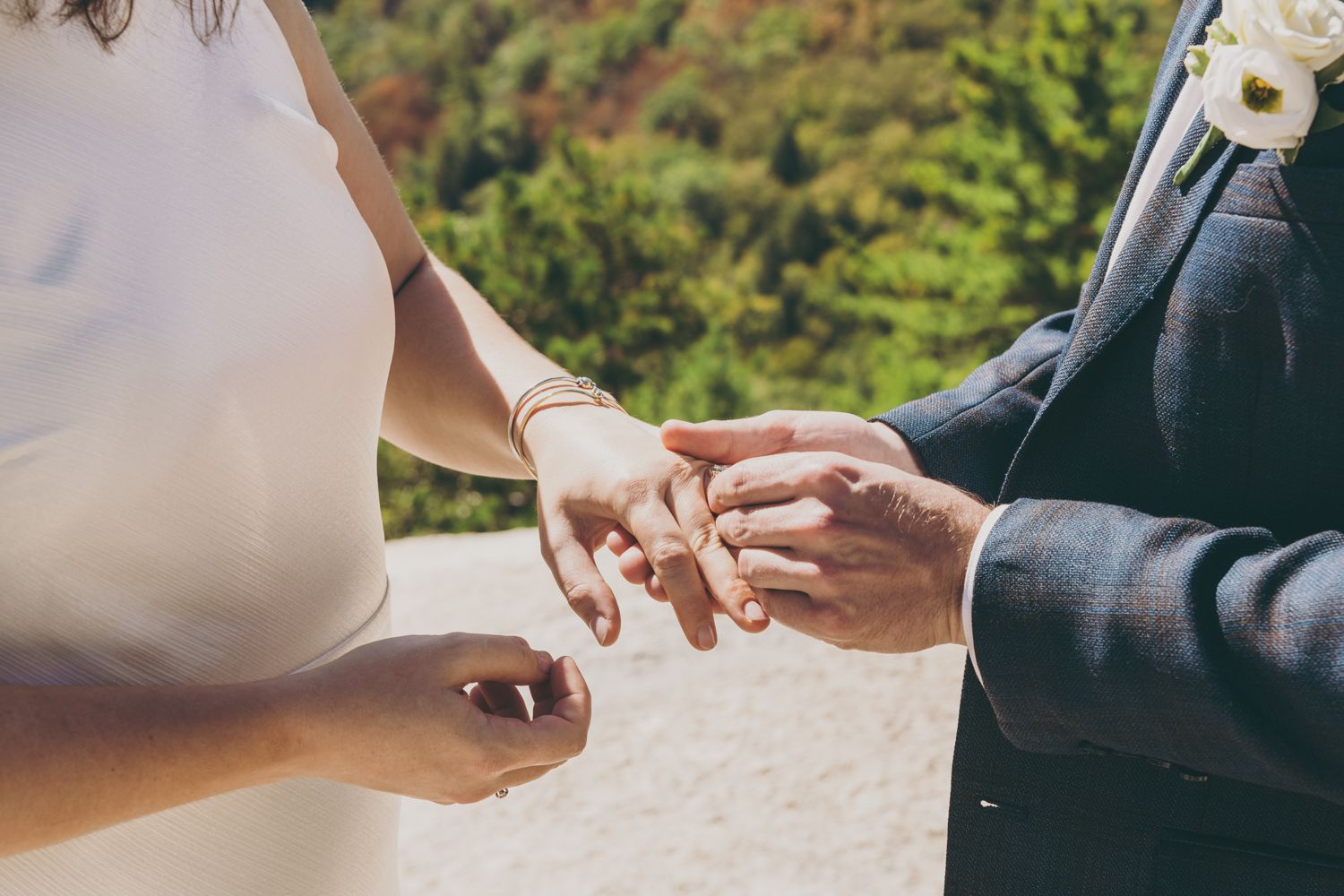 Groom places wedding ring on brides finger during outdoor mountain ceremony.
