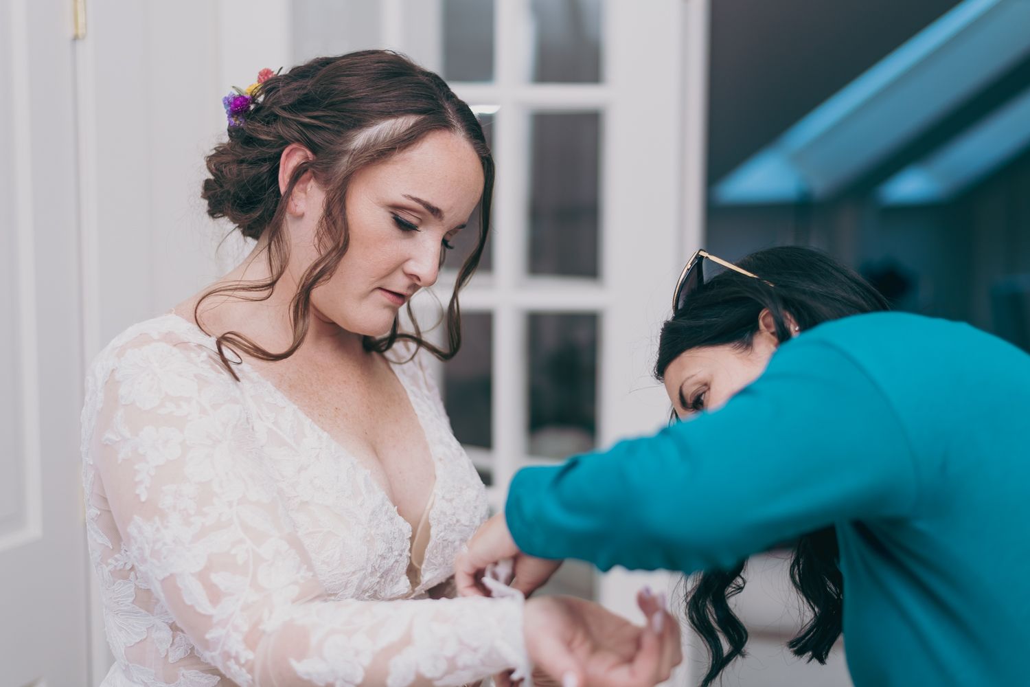 Wedding assistant helping bride in lace gown with dress details before the ceremony.
