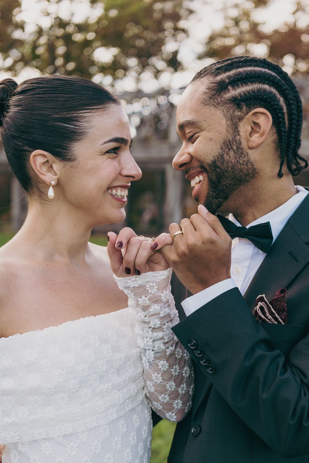 Happy bride and groom in formal wedding attire smiling at each other while holding hands outdoors.