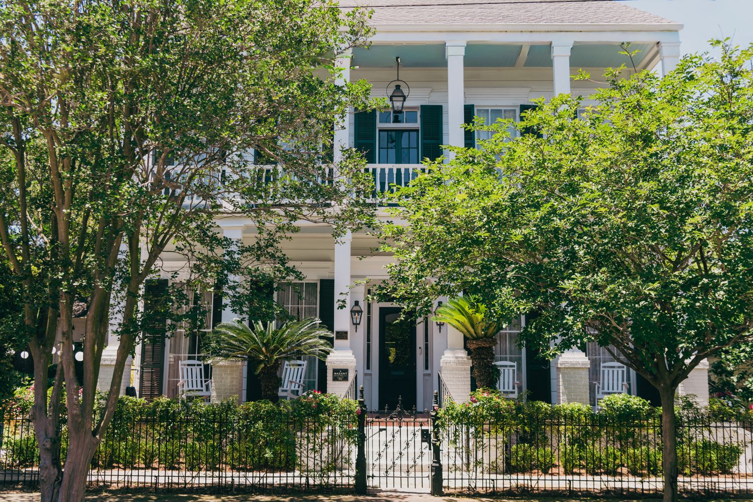 Elegant white two-story Southern home with grand columns, black shutters, and iron gate entrance.