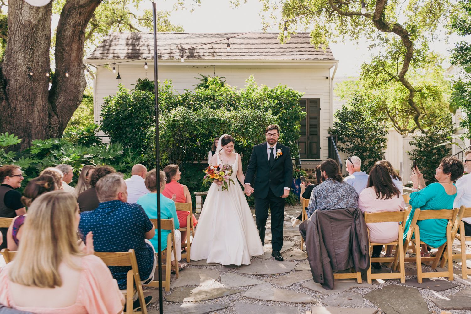 Newlyweds walk back down the aisle hand in hand after their outdoor garden wedding ceremony.