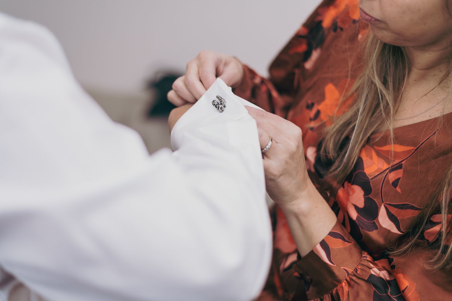 Bride adjusting groom's cufflink on white suit sleeve before wedding ceremony.